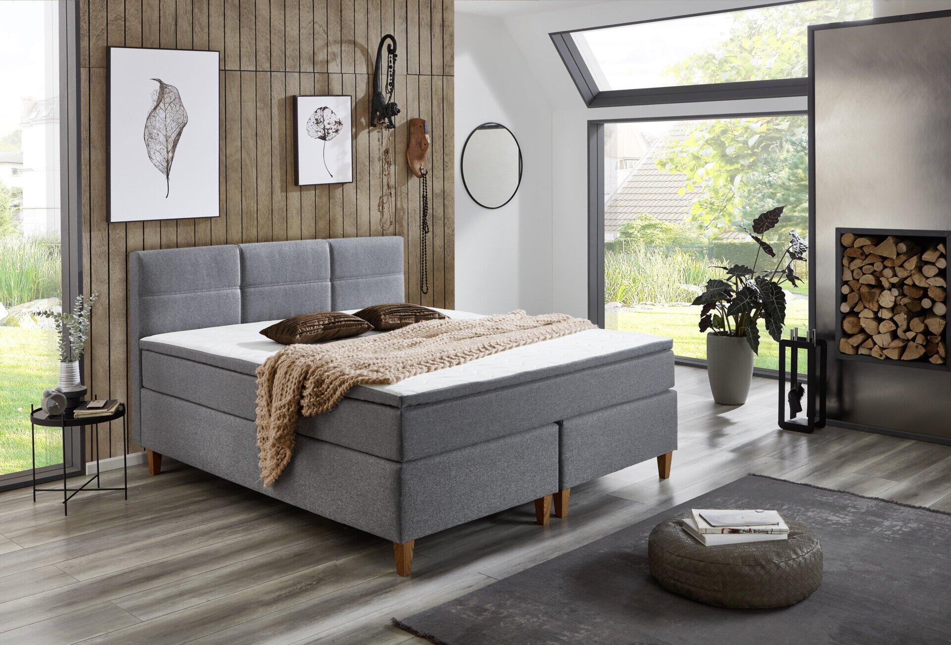 Boxspringbett Kenora BX2360 mit grauem Stoffbezug, hochgestecktem Kopfteil und integrierter Aufbewahrungslösung, abgebildet in einem stilvollen Schlafzimmer.