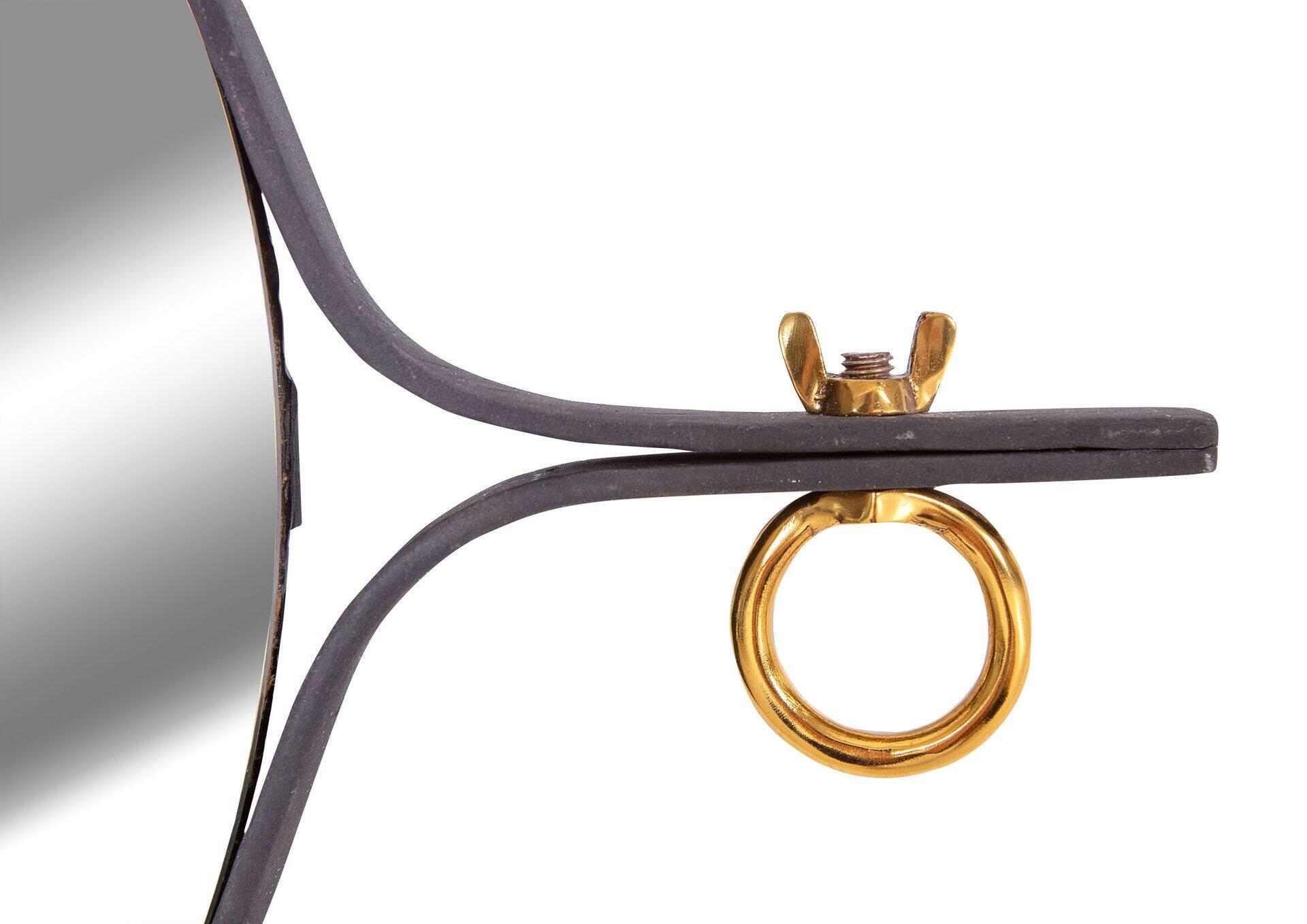 Detailaufnahme des Camilla-Spiegels mit trapezförmigem, dunklem Metallrahmen und goldenem Aufhängeelement mit Verschlussmutter.