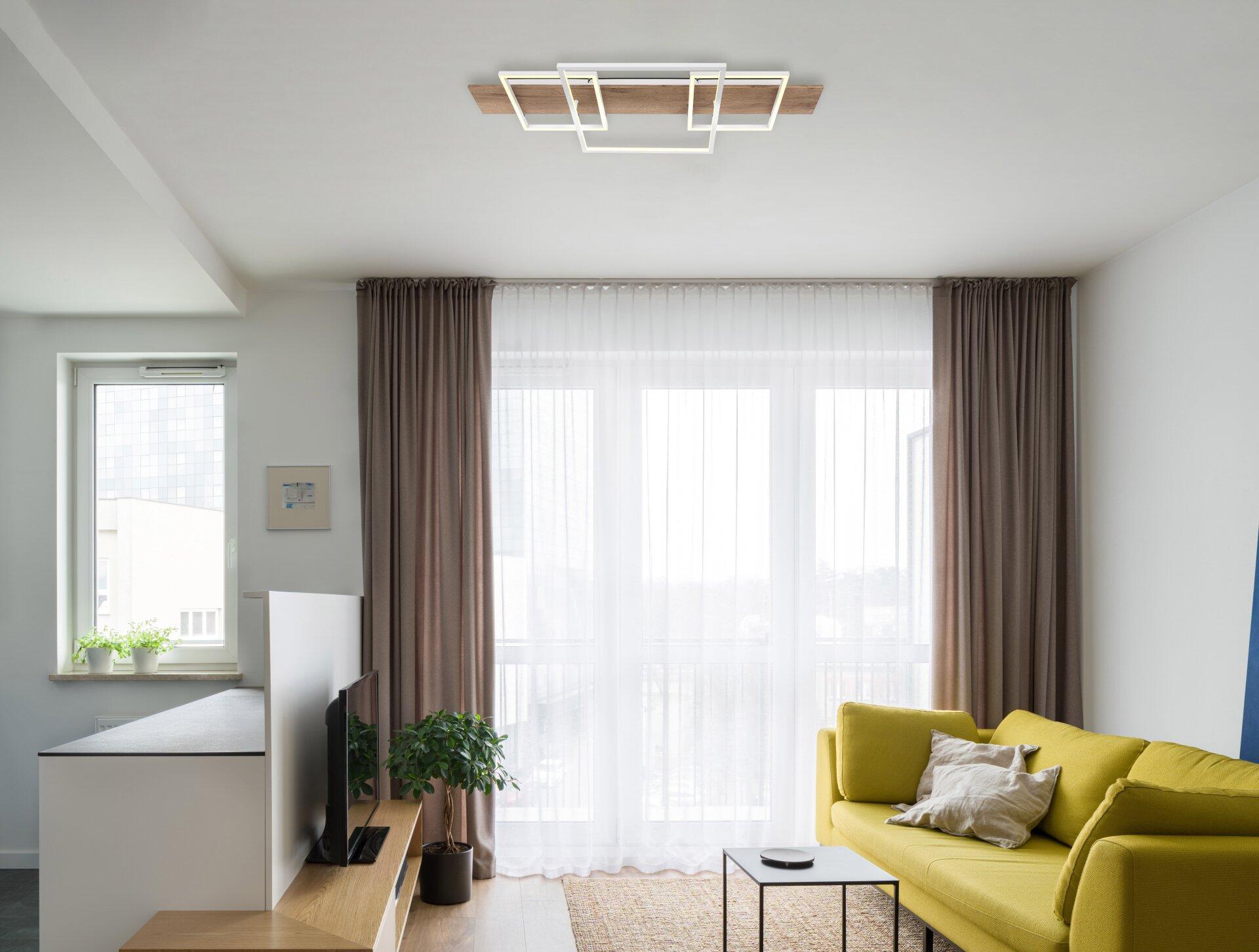 Deckenleuchte VANNIE I mit weißem Rahmen und holzfarbenem Lichtdiffusor, integriert in ein modernes Wohnzimmer und aus leicht erhöhter Perspektive fotografiert.