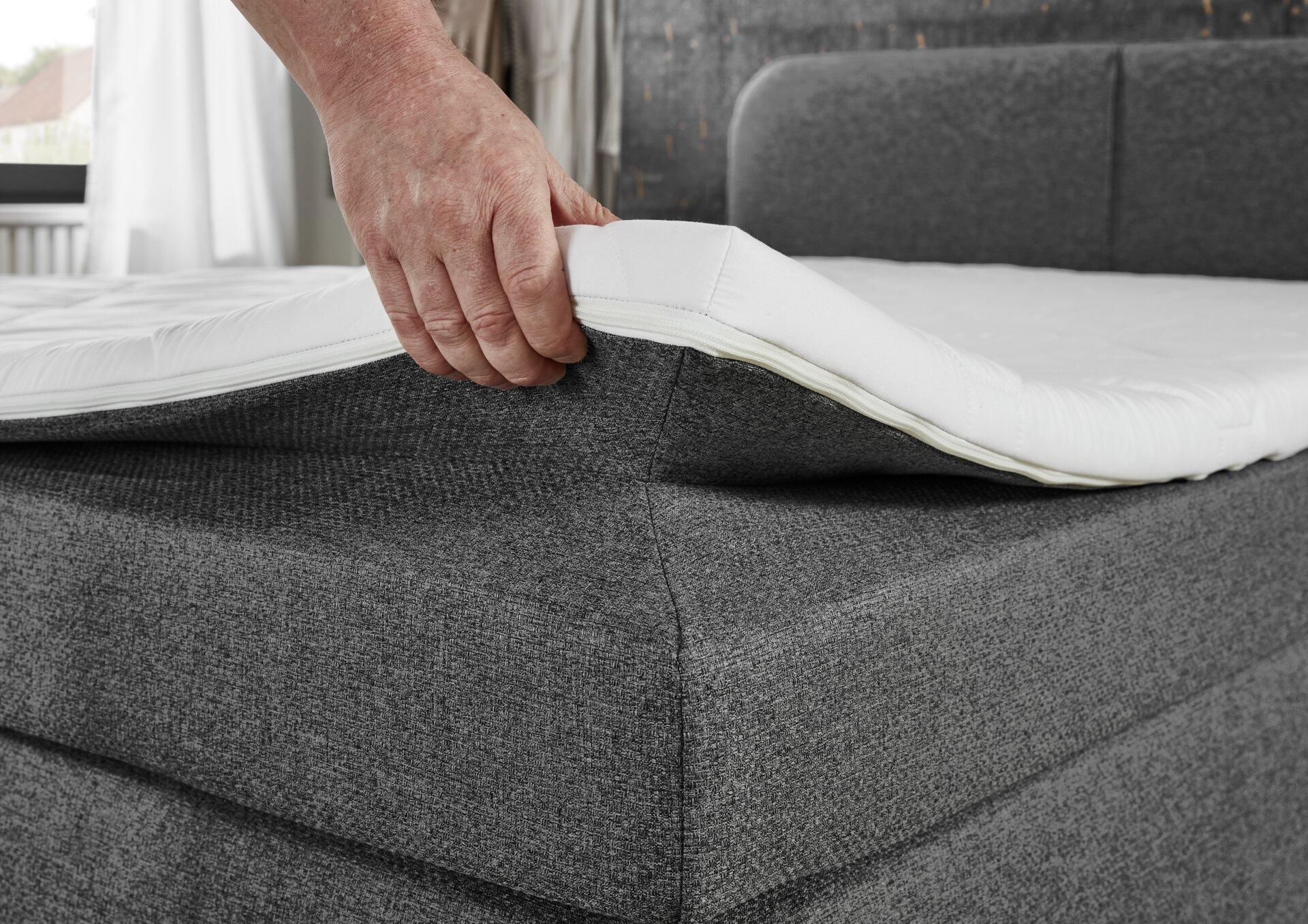 Seitenansicht eines Boxspringbettes Joliet BX2410 mit Komfortschaum-Topper und grau-anthrazitfarbener, gepolsterten Bettgestell-Polsterung, die die Tiefe des Bettes betont.