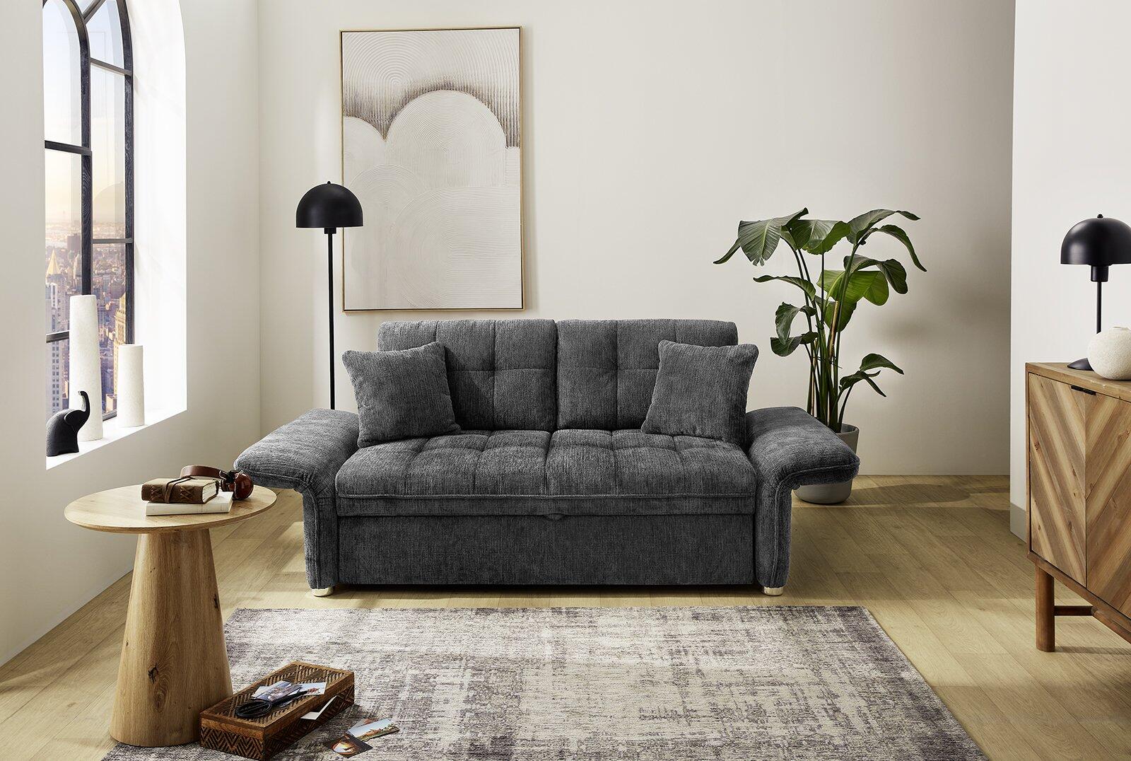 Schlafsofa Leon mit horizontaler Riegelstruktur im Rückenbereich und abgerundeten Armlehnen, präsentiert auf einem hellen Holzboden vor städtischer Kulisse.