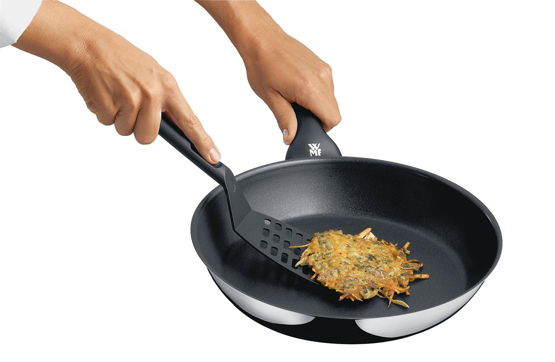 WMF Pfannenwender: Detailaufnahme einer Hand, die mit einem Pfannenwender Kartoffeln und Gemüse in einer runden Bratpfanne mit gebogenem Rand und geripptem Boden anhebt.