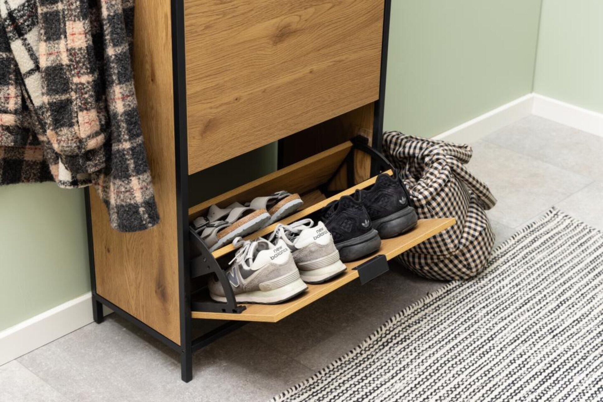 Schuhschrank Seaford in Wildeiche mit schwarzem Metallrahmen und Dreiviertelperspektive, die Fächer mit Klappläden und verschiedene Sneaker-Modelle zeigt.
