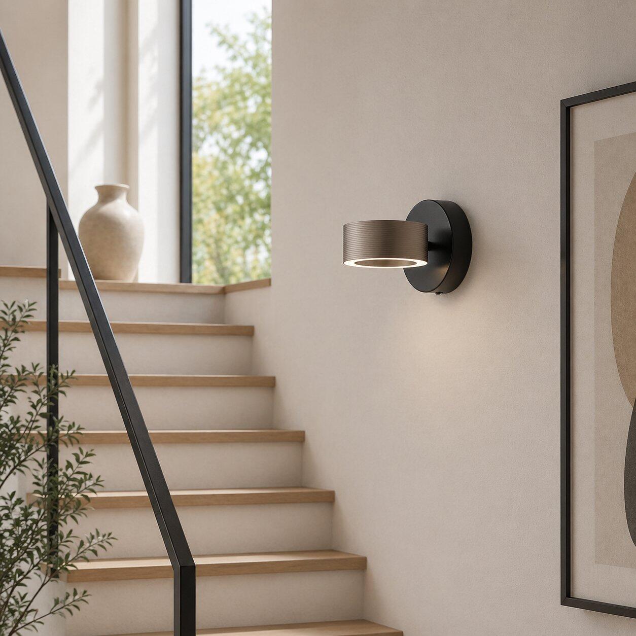 Wandleuchte Axion mit schwenkbarem Kopf und integriertem Druckschalter, dargestellt in einem modernen Raum mit Blick in den Garten und leicht erhöhter Perspektive.