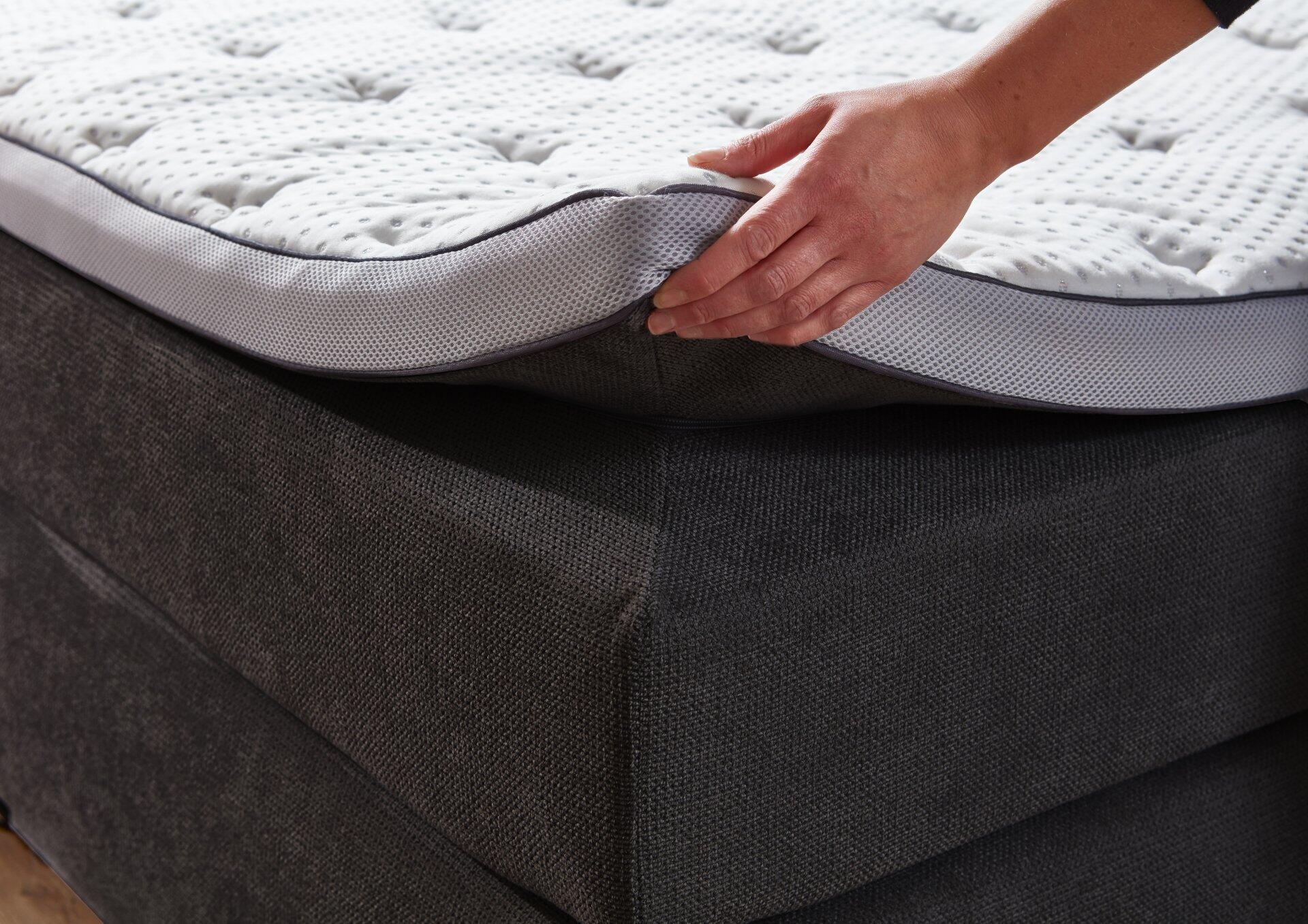 Detailaufnahme des Boxspringbettes Portage BX2110 aus Vogelperspektive, die die mehrschichtige Matratzenkonstruktion mit Schaumstoffgitter und Topper sowie den grauen Stoffbezug zeigt.