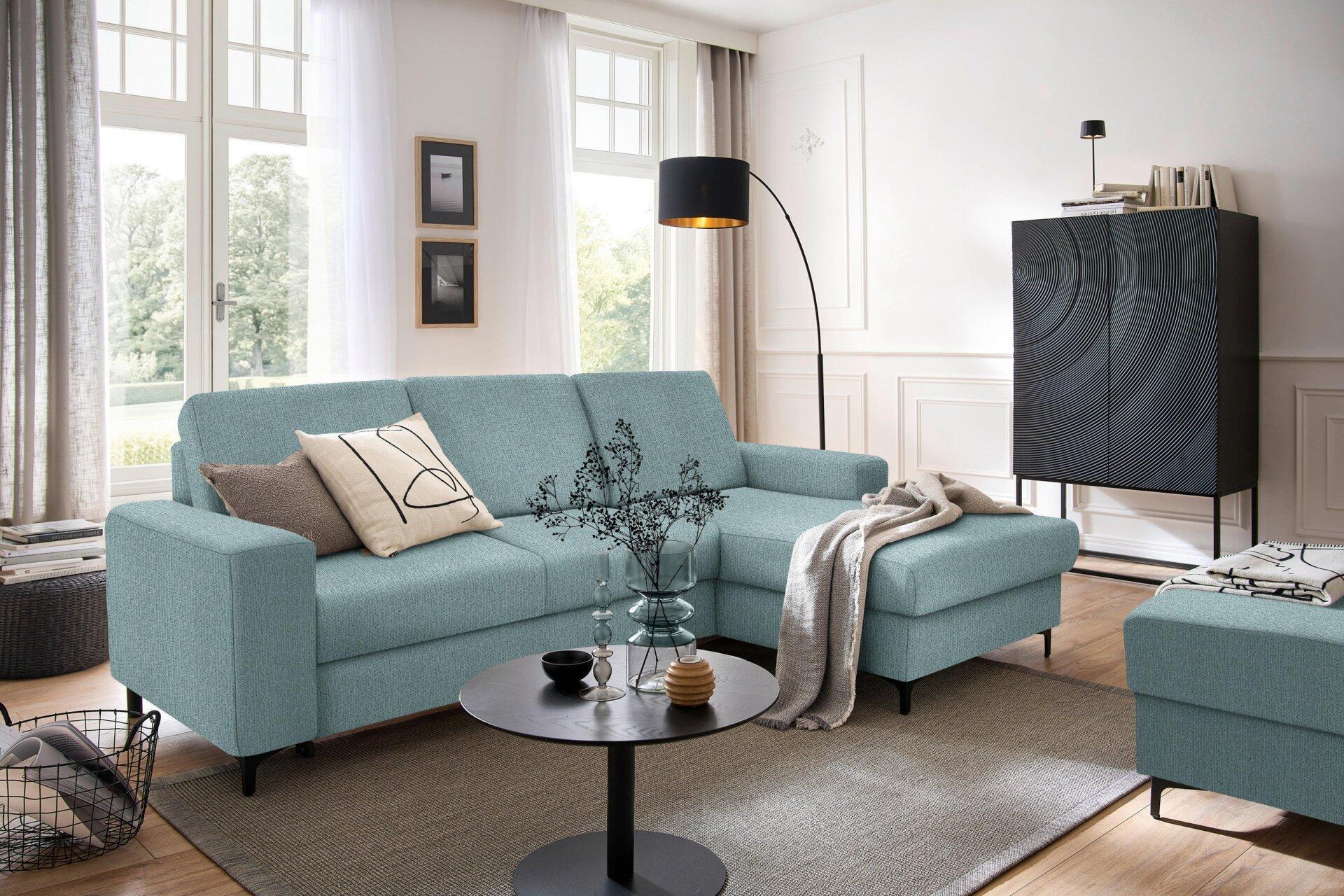 Ecksofa Balina mit rechts liegender Ottomane und ausgezogener Schlaffläche, dargestellt in einer hellen Wohnzimmer-Szene mit schwarzen Metallfüßen und niedrigem Korpus.