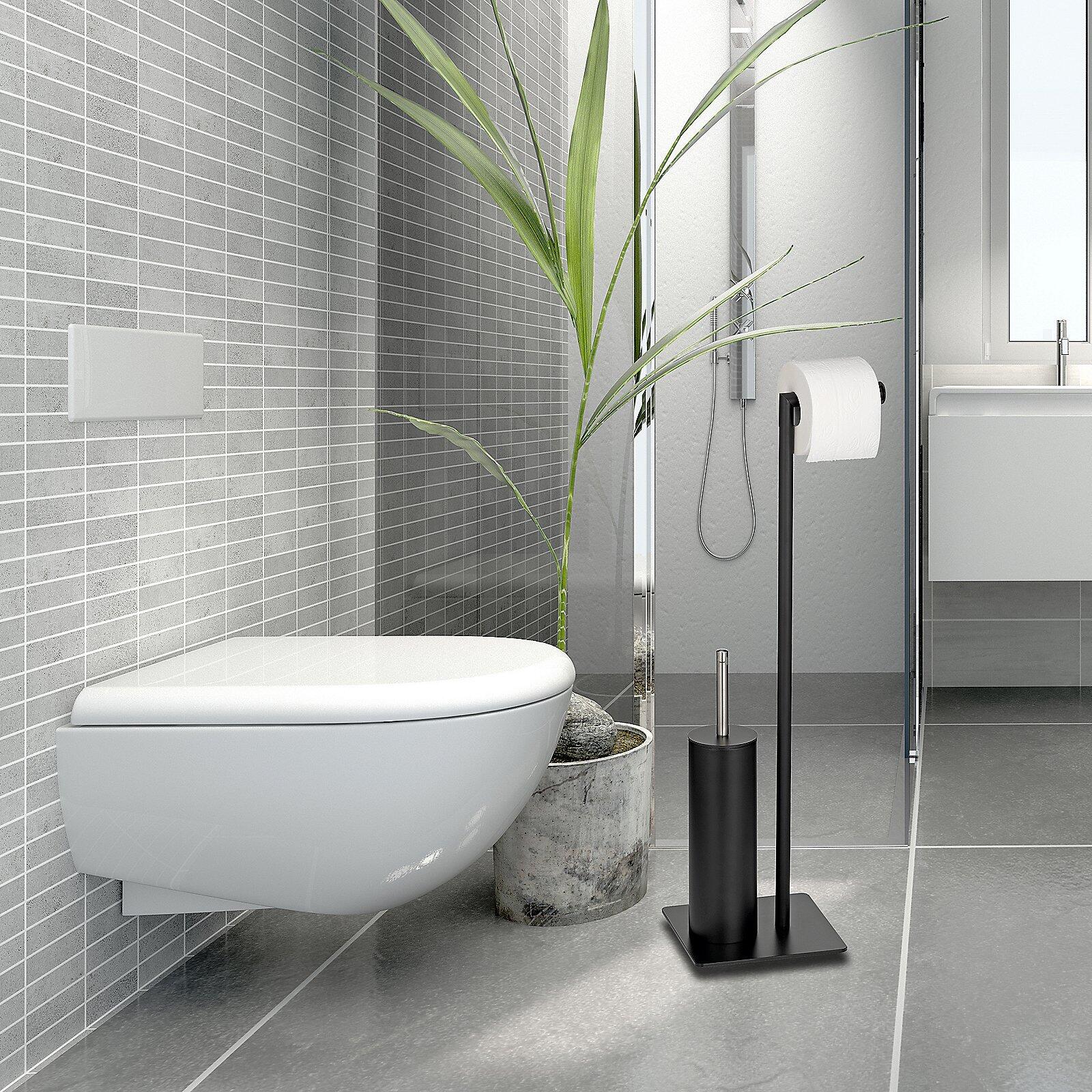 Toilettengarnitur Style mit schwarzer Toilettenpapierhalterung auf quadratischem Sockel, schräg zur Wandtoilette und Pflanze im grauen Topf.