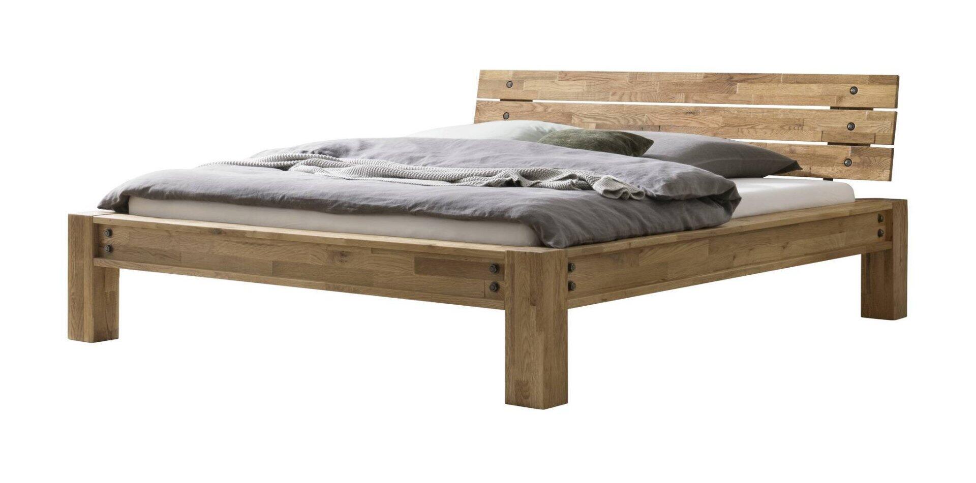 Bett San Simeon aus hellem Holz mit erhöhten Füßen und Kopfstütze, abgebildet in einer Übersichtsperspektive mit weißer Bettwäsche und Accessoires.