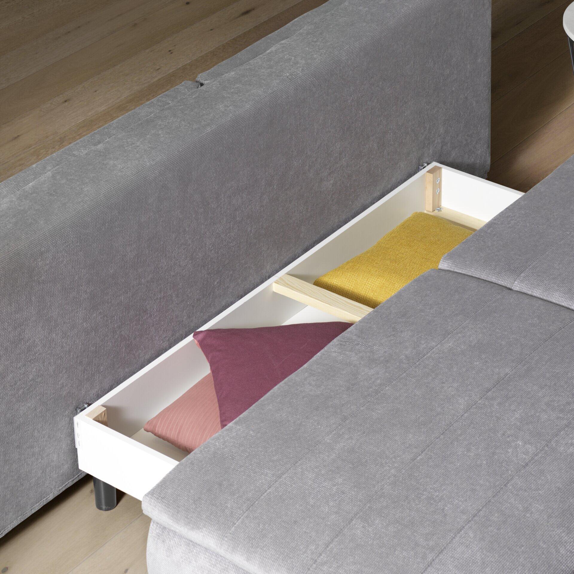 Nahaufnahme des Stauraums des Boxspringsofas Melly mit weißem Innenraum, Holz-Einlegetrennungen und bunten Kissen.