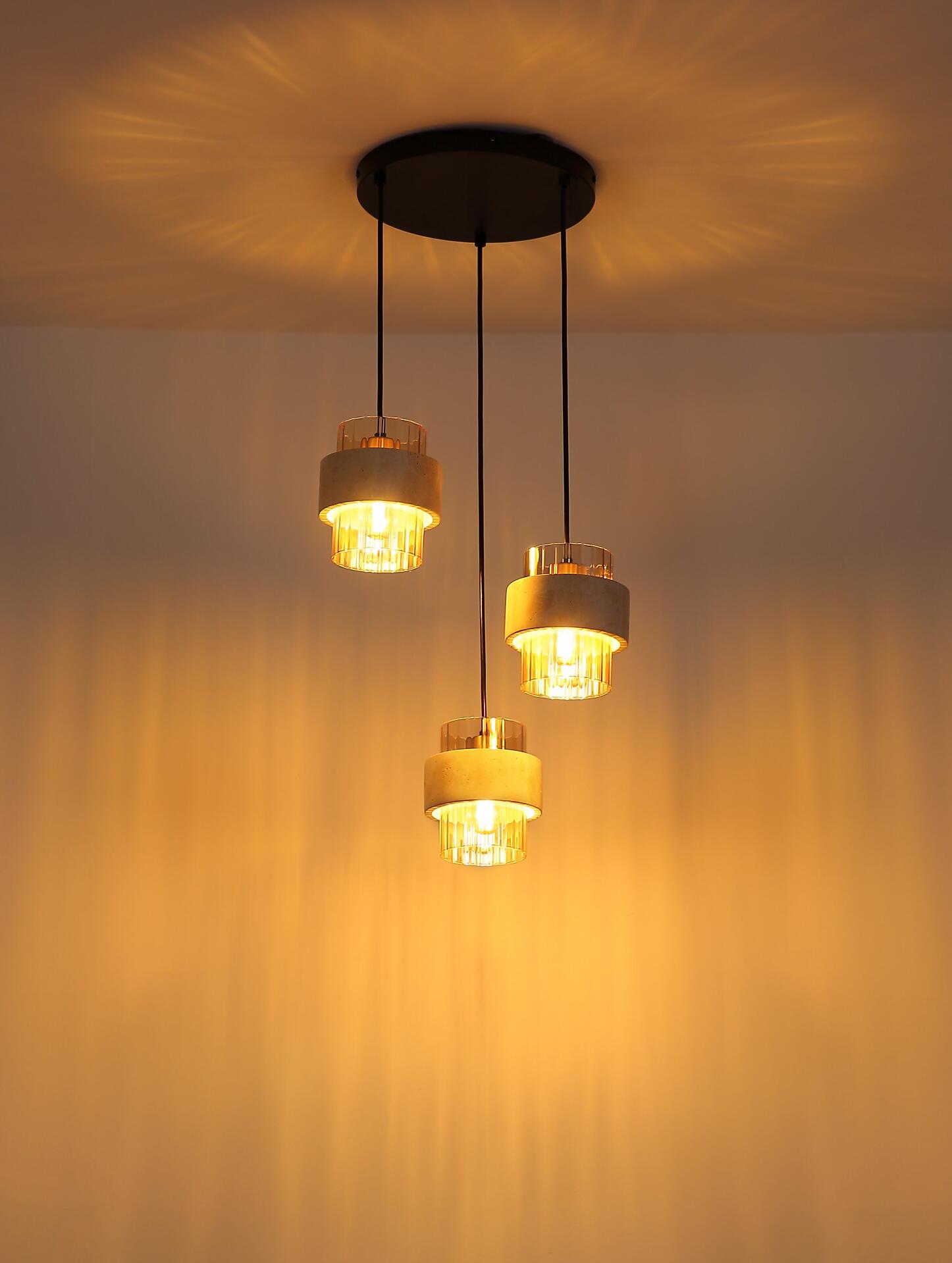 Dreifache Pendelleuchte DAREN mit goldenen Ringen und bernsteinfarbenen Glaskugeln, die warmes Licht reflektiert und durch unterschiedliche Höhen eine dynamische Optik erzeugt.