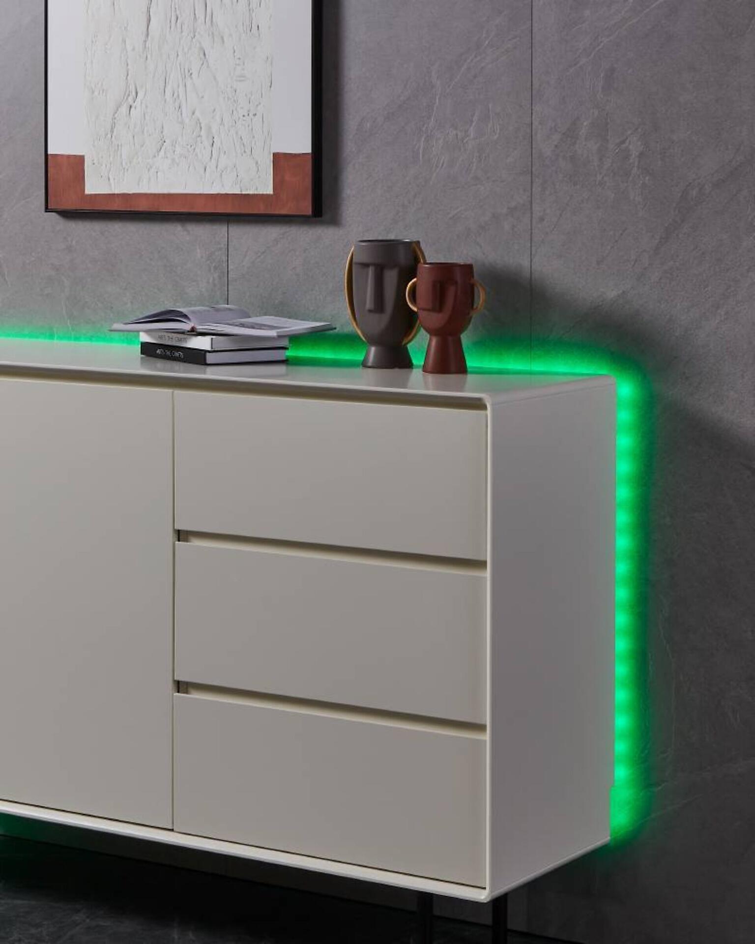 Weißes LED-Kommodenschrank "Stripe, Led Stripe-Z" mit drei Schubladen, silberfarbenen Griffen und grüner LED-Hintergrundbeleuchtung, dargestellt in einer Frontansicht.
