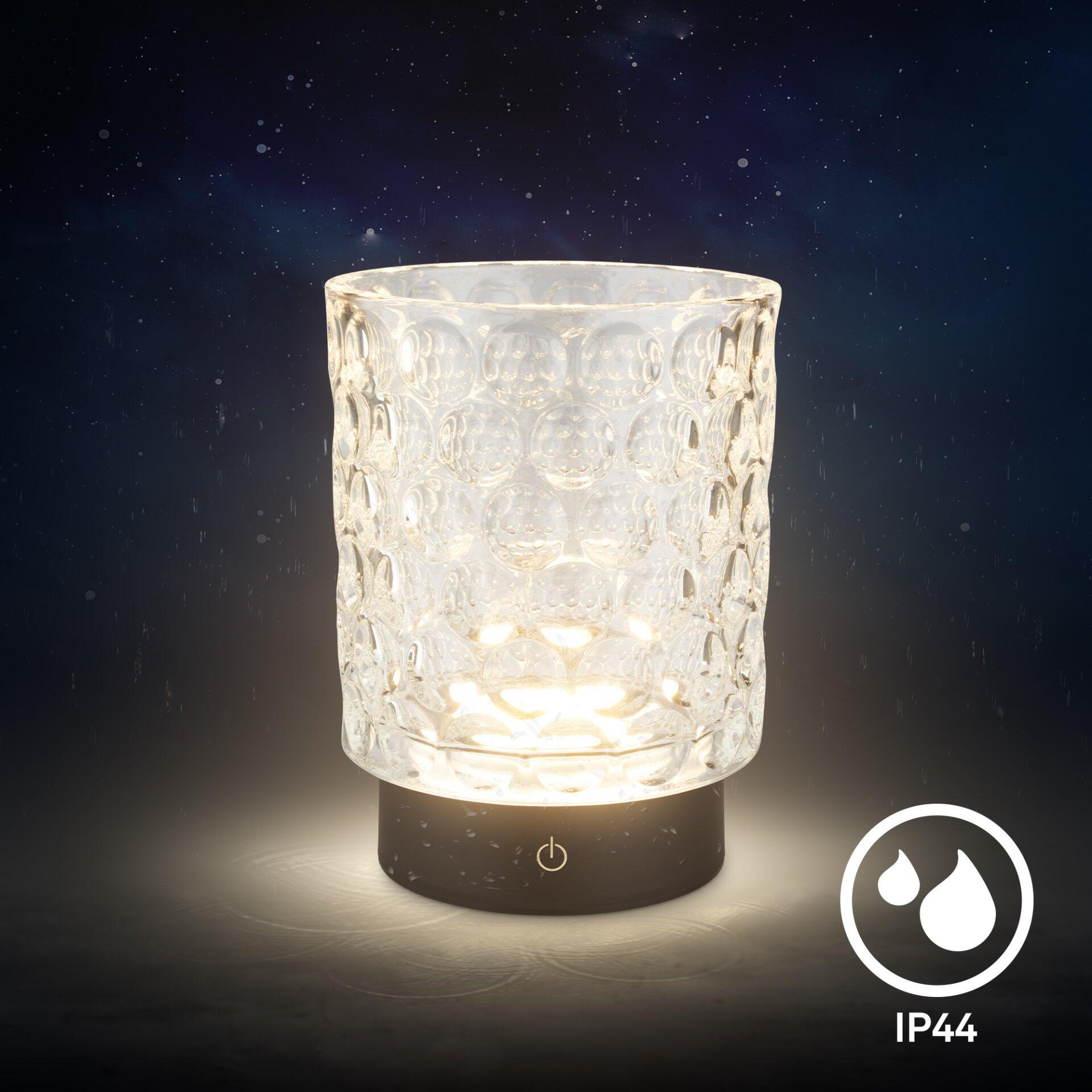Tischleuchte Sunora mit transparentem, wellenförmigem Lampenschirm und Touchdimmer, dargestellt in Frontalperspektive mit warmem Licht und Spritzwasserschutz.