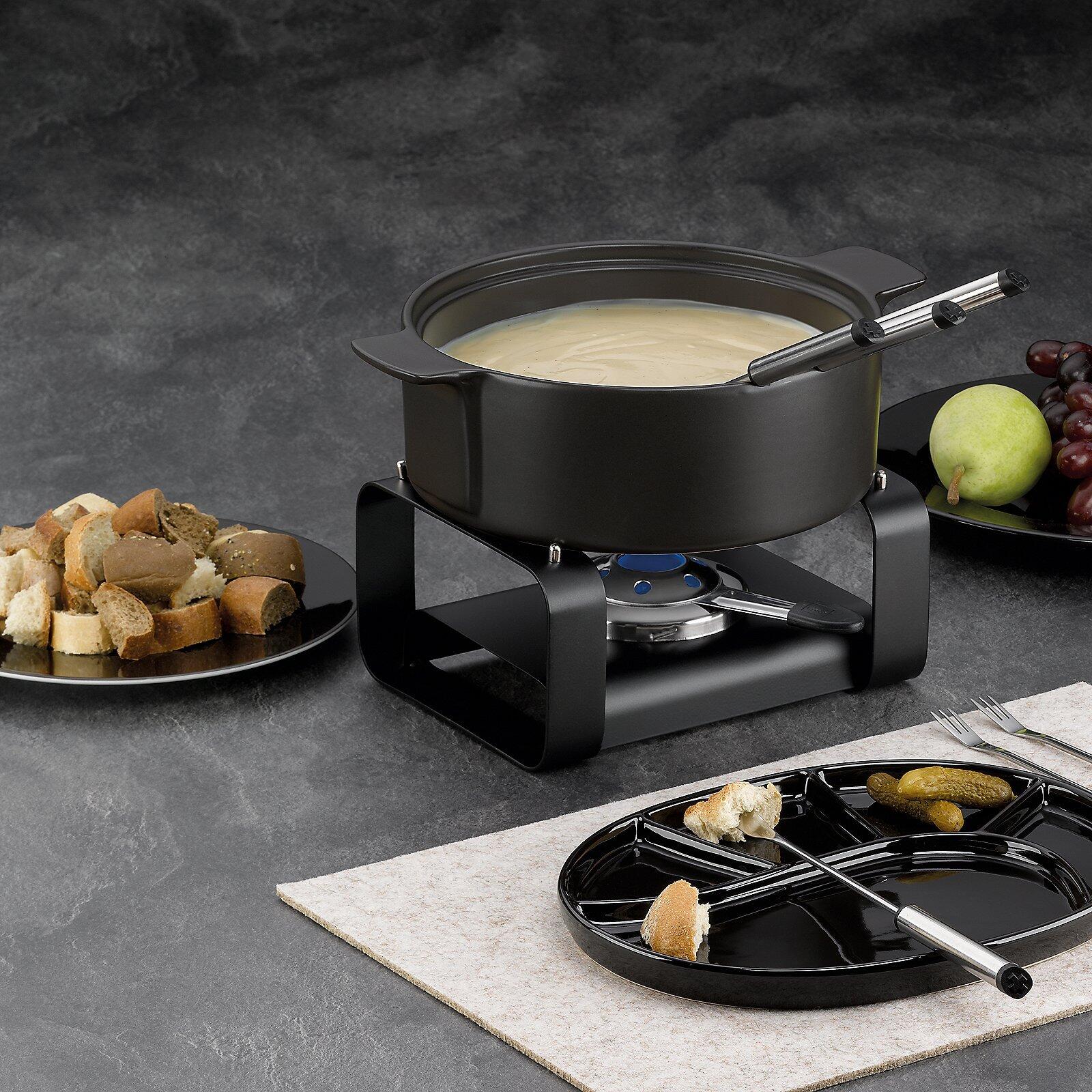Fondue-Set "Roman" mit geschmolzenem Käse, Schöpflöffel und Beilagen auf einer grauen Unterlage, präsentiert als geselliges Esserlebnis.