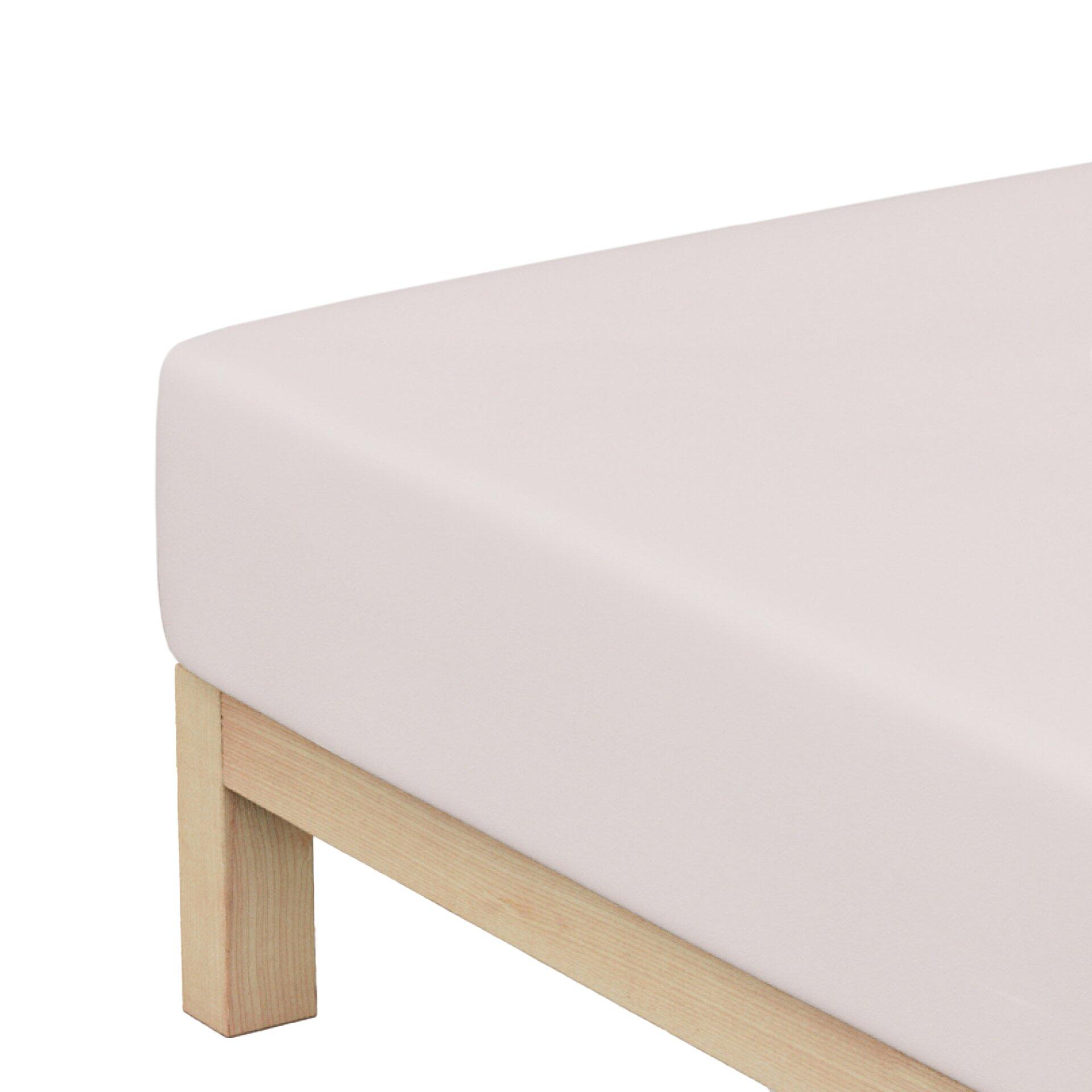 Detailaufnahme eines hellrosa Spannbetttuchs aus Mako-Jersey, das auf einem Sofa oder Sessel drapiert ist und die Struktur der darunterliegenden Holzkonstruktion zeigt.