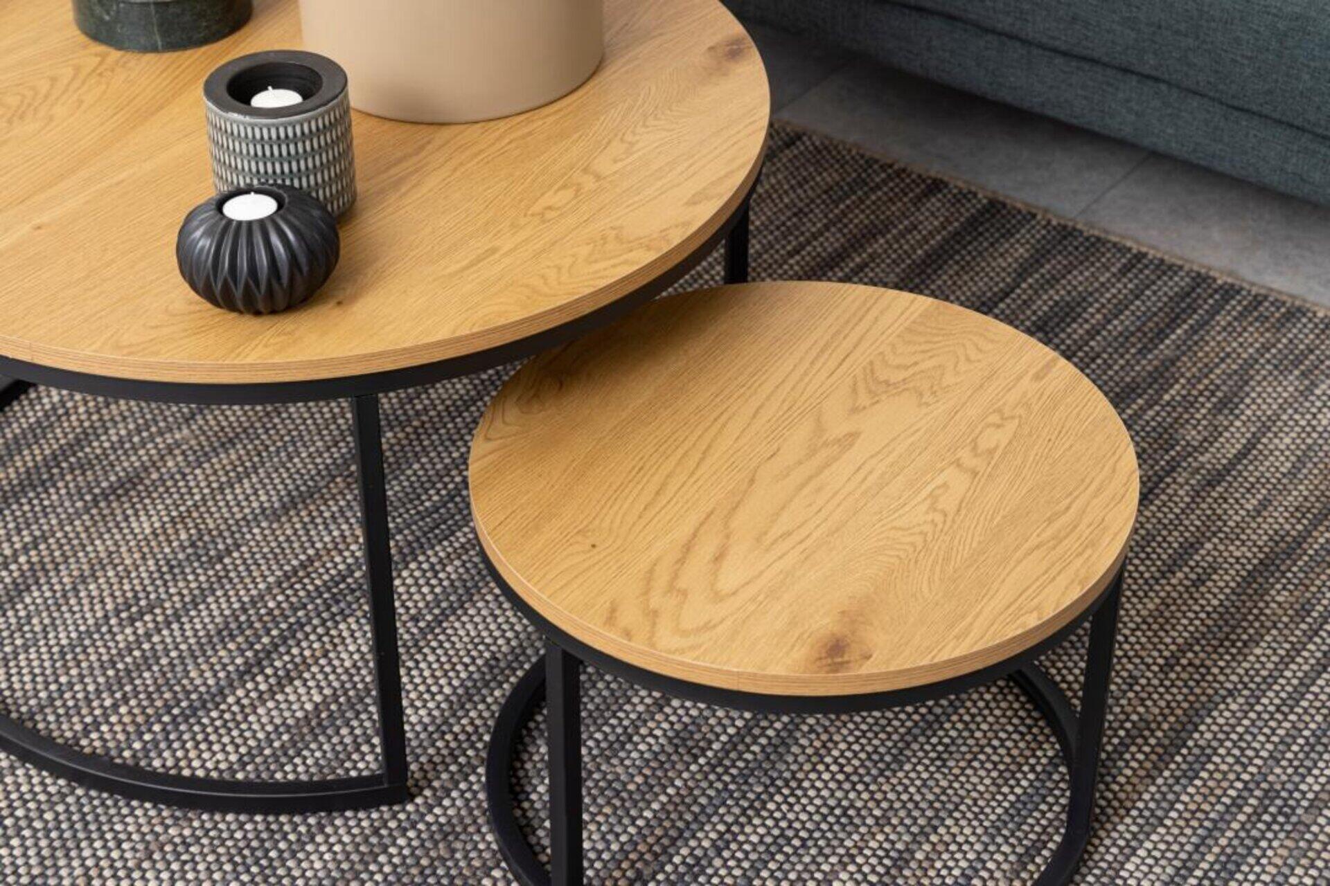 Couchtisch Spiro: Set aus zwei stapelbaren Couchtischen mit heller Holzbeschichtung und schwarzem Metallring, dargestellt ineinandergreifend vor einem Sofa.