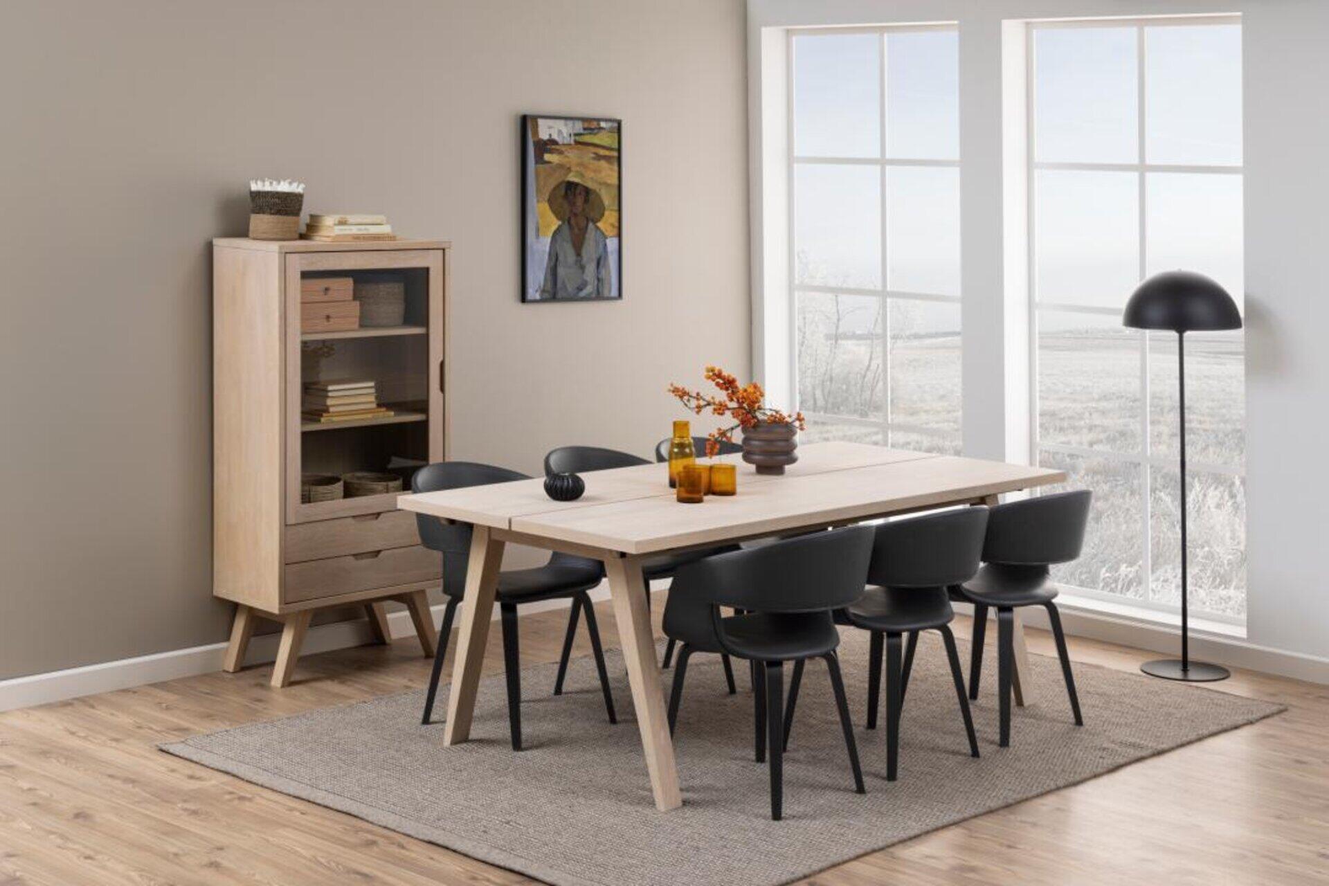 Esszimmer mit Esstisch A-Line, der eine Splittop-Optik und schräge Beine aufweist, sowie sechs schwarze Stühle und angrenzende Einrichtung.