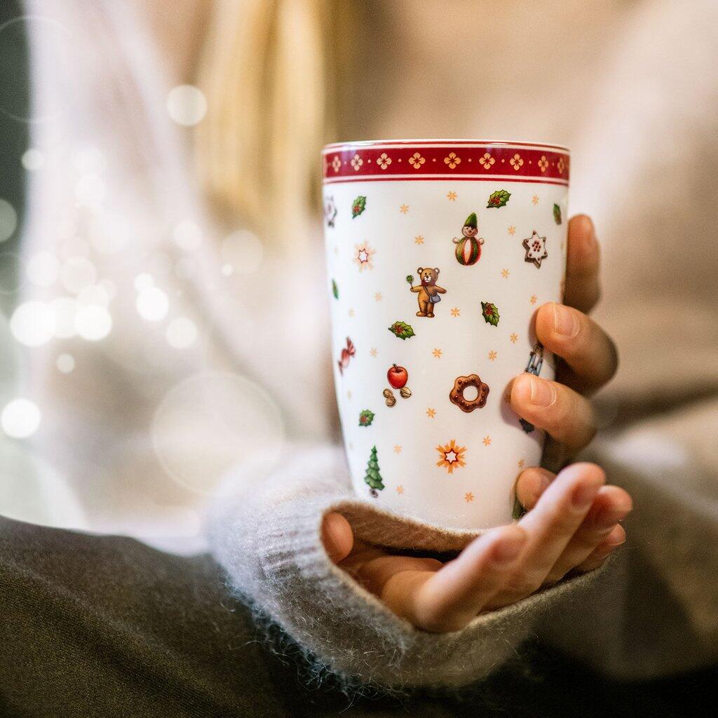 Weihnachtlicher Kaffeebecher "Toys Delight" von Villeroy & Boch in den Händen, zeigt ein festliches Dekor mit Bären, Sternen und Christbäumen.