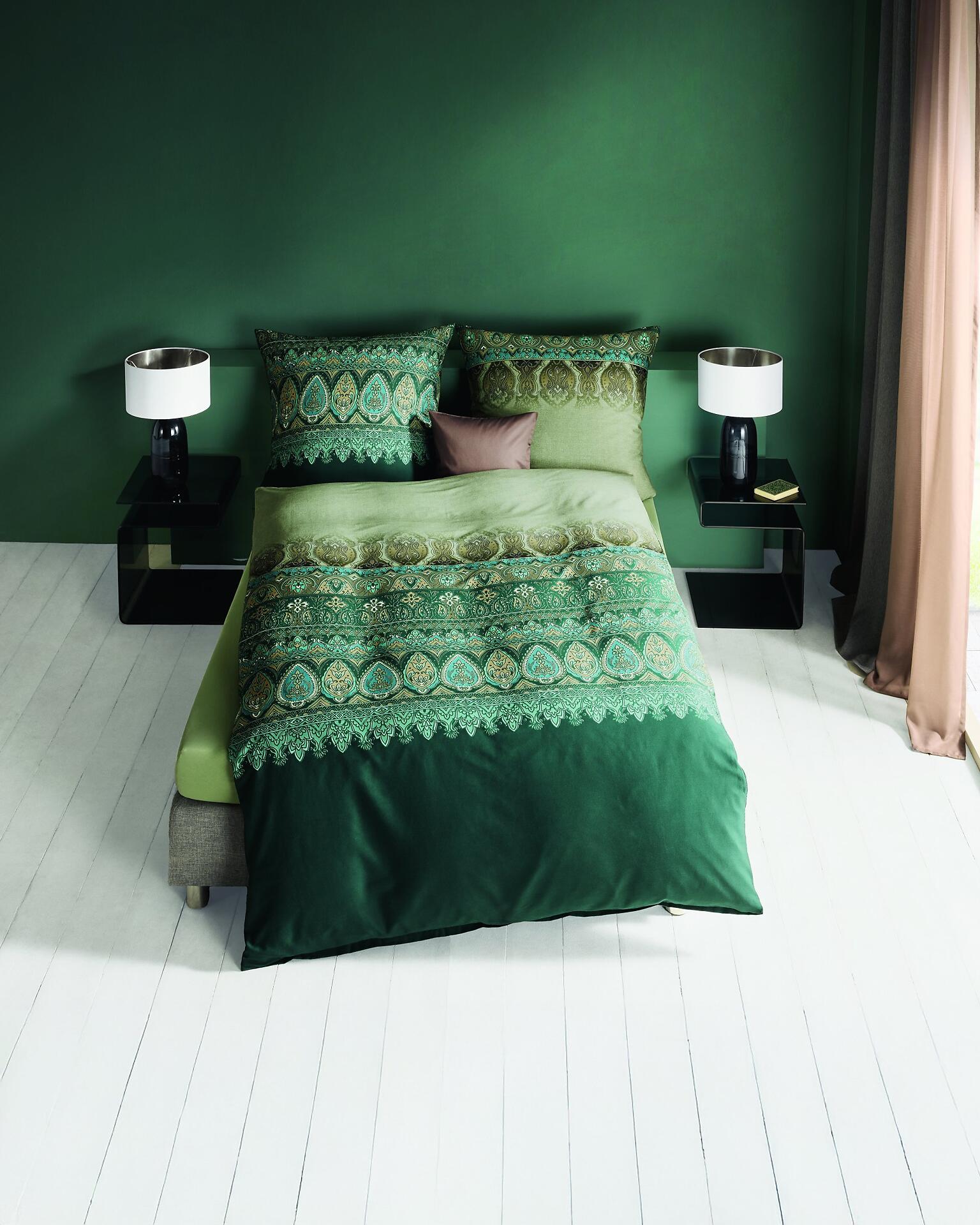 Dunkelgrüne Bettwäsche Opulence mit goldenem Muster und passenden Kissen auf einem stilvollen Bett in einem Schlafzimmer.