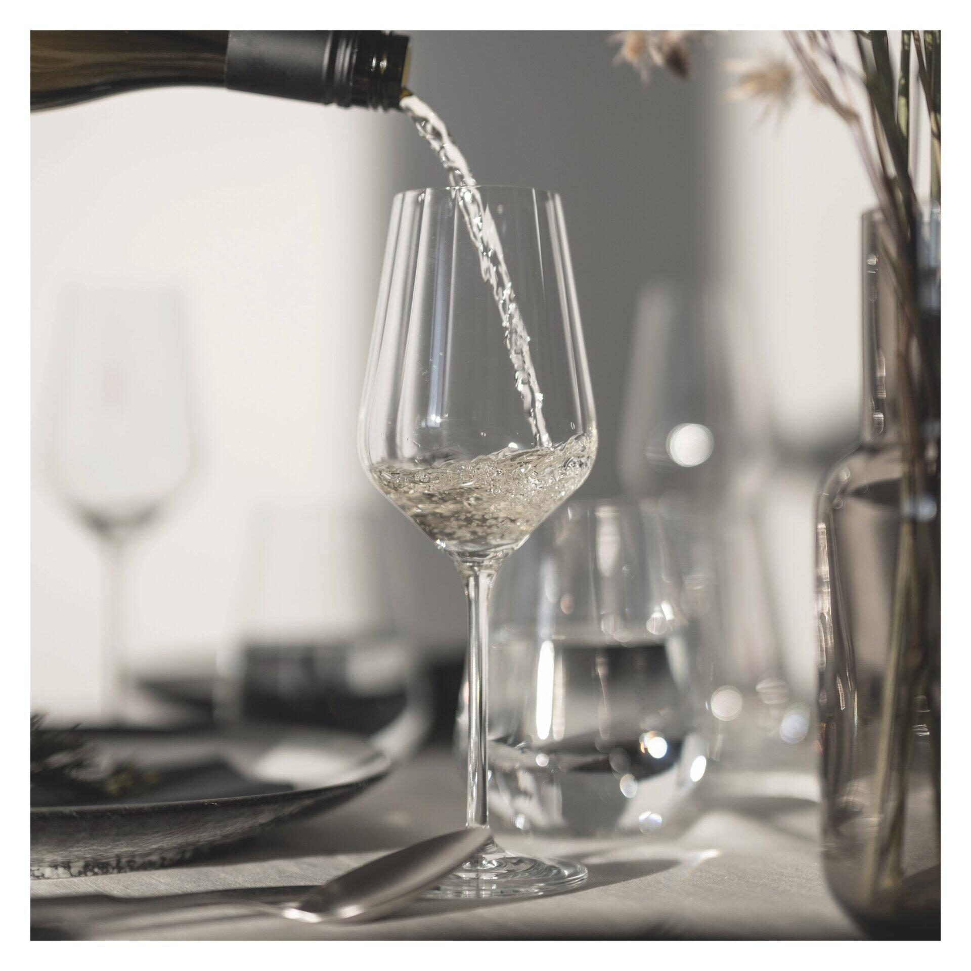Nahaufnahme eines Weißweinglases, in das Wein fließt, präsentiert in stilvoller Szene mit gedecktem Tisch.