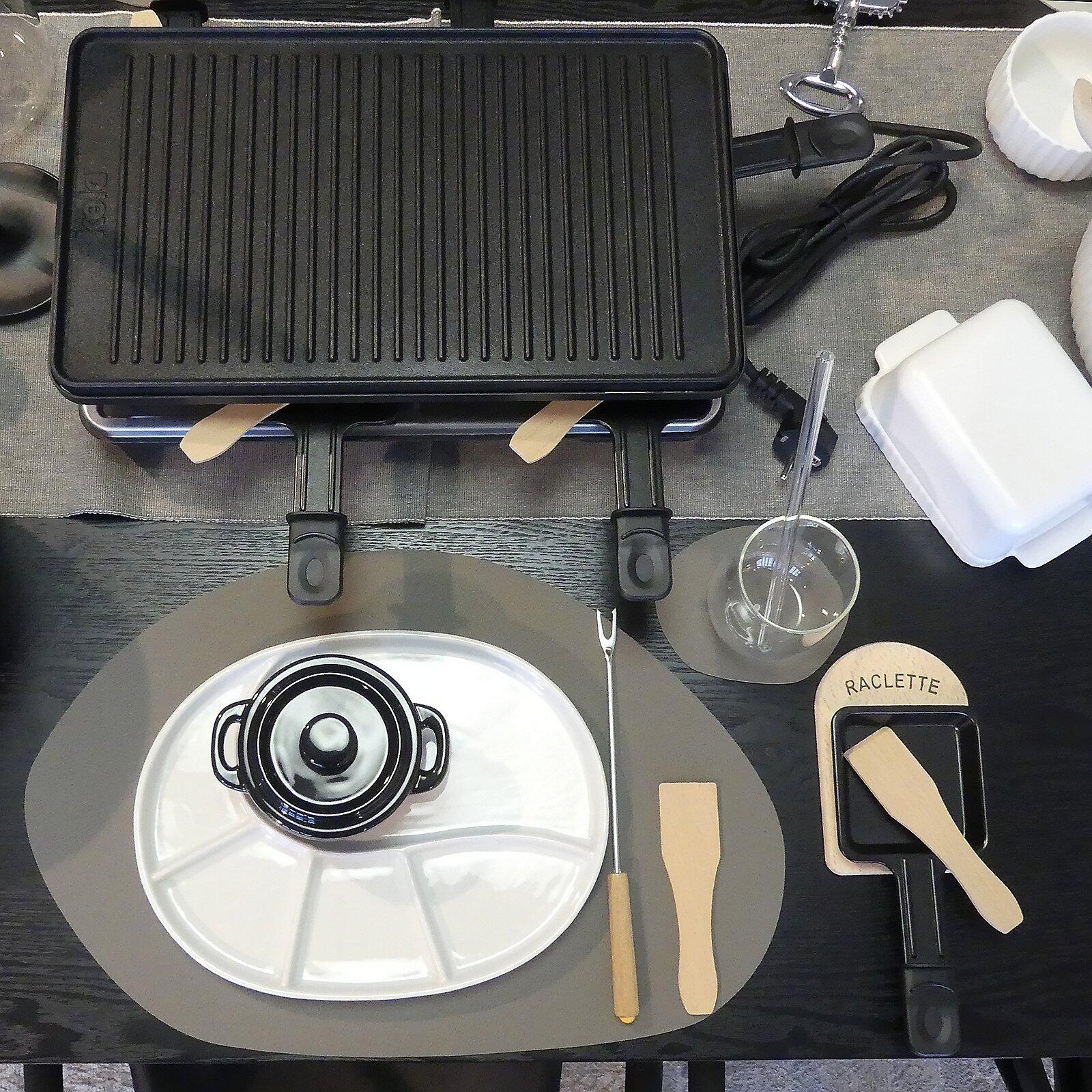 Raclette-Brettchen Baar mit vier Pfännchen für Raclettekäse und vier Spateln auf einem Gestell.