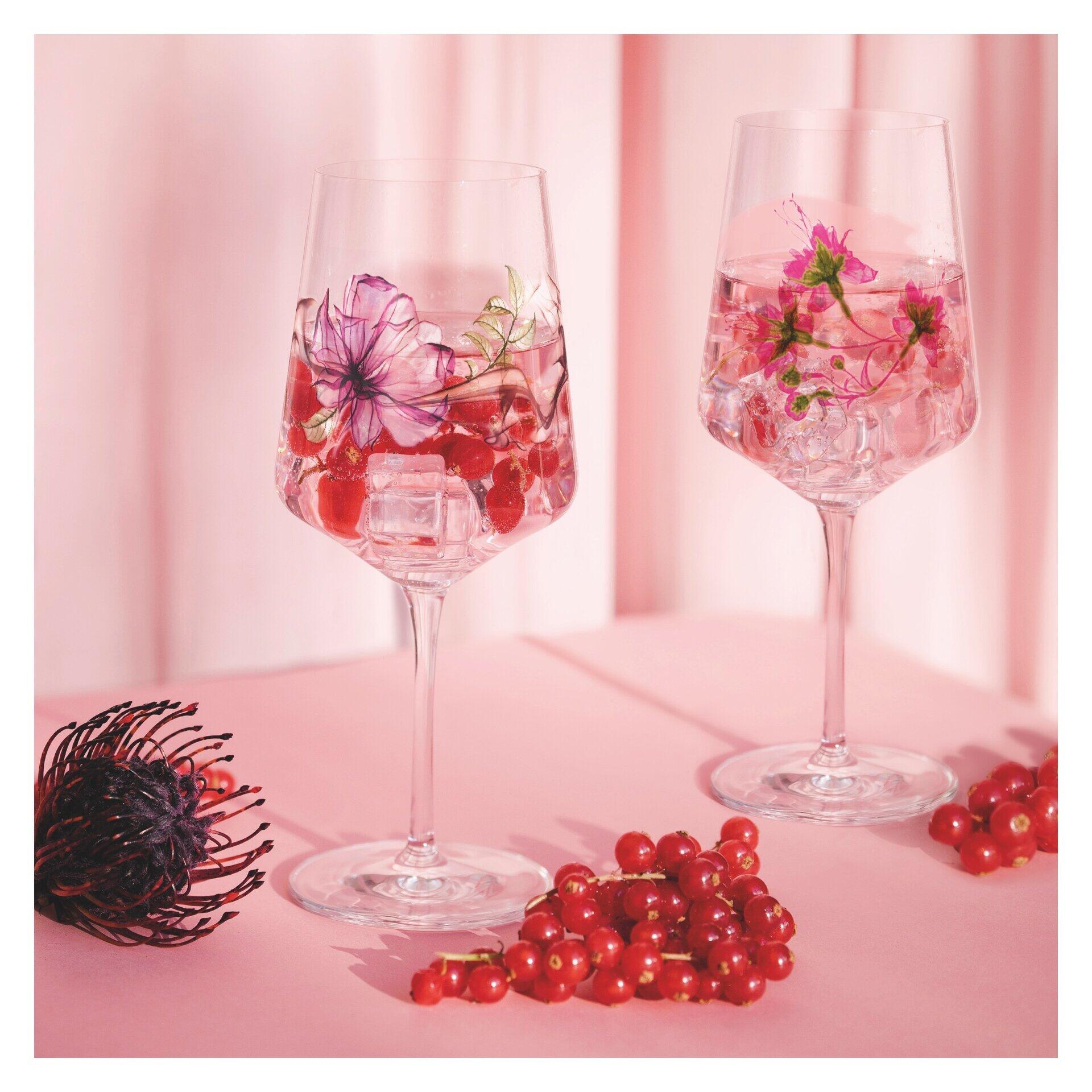Zwei Aperitifgläser im Oleander-Fuchsie-Design mit sommerlichen Blüten und Eiswürfeln, präsentiert in einer hellrosa Umgebung.