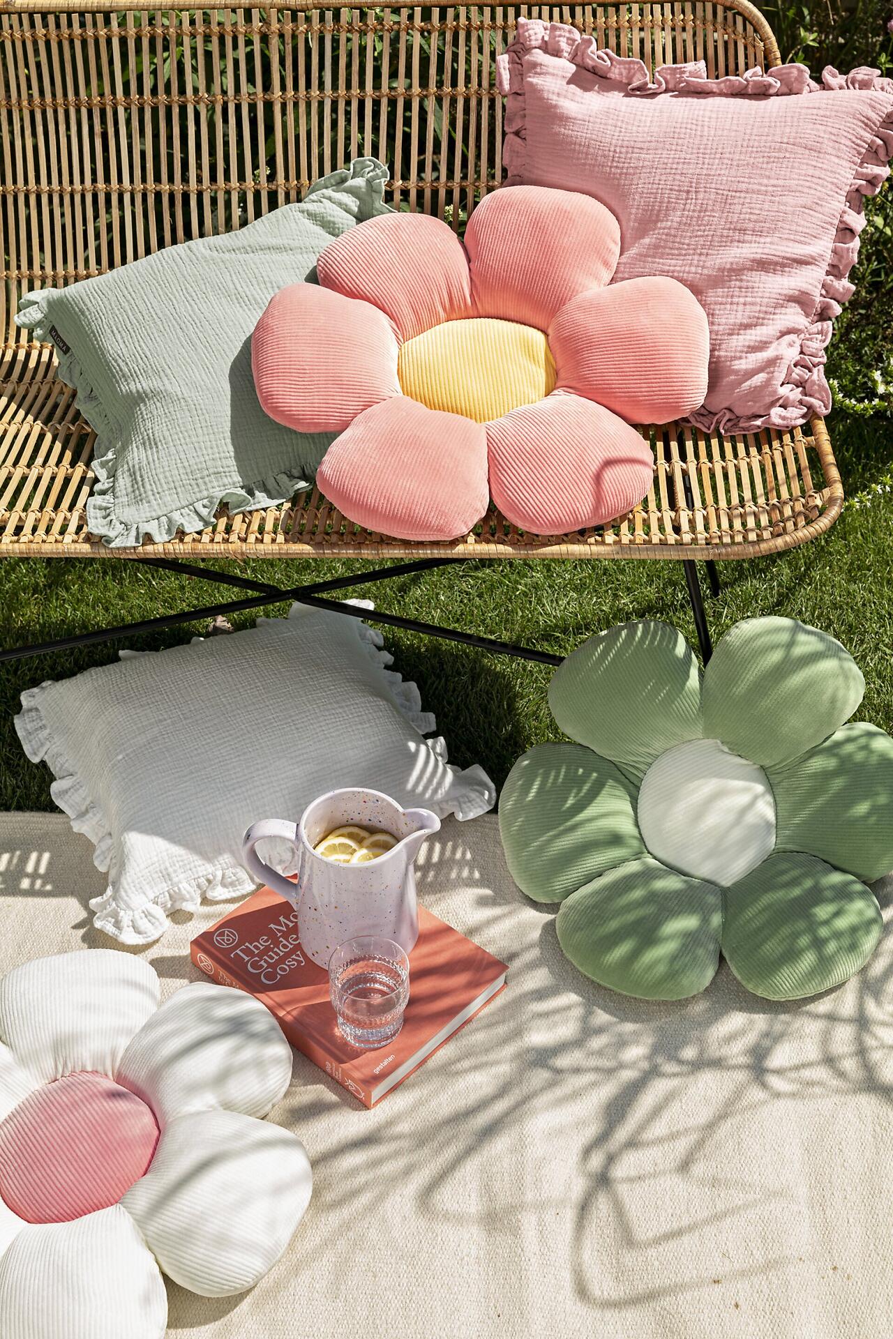 Formkissen Minnie, gelbes Cordsamt-Kissen in Blüteform, stilvoll arrangiert vor einem Rattan-Sessel.