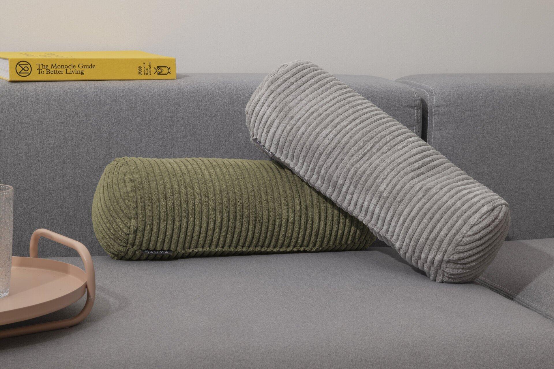Dekorative Nackenrolle Shara in Grünton mit vertikaler Cordstruktur auf einem grauen Sofa.