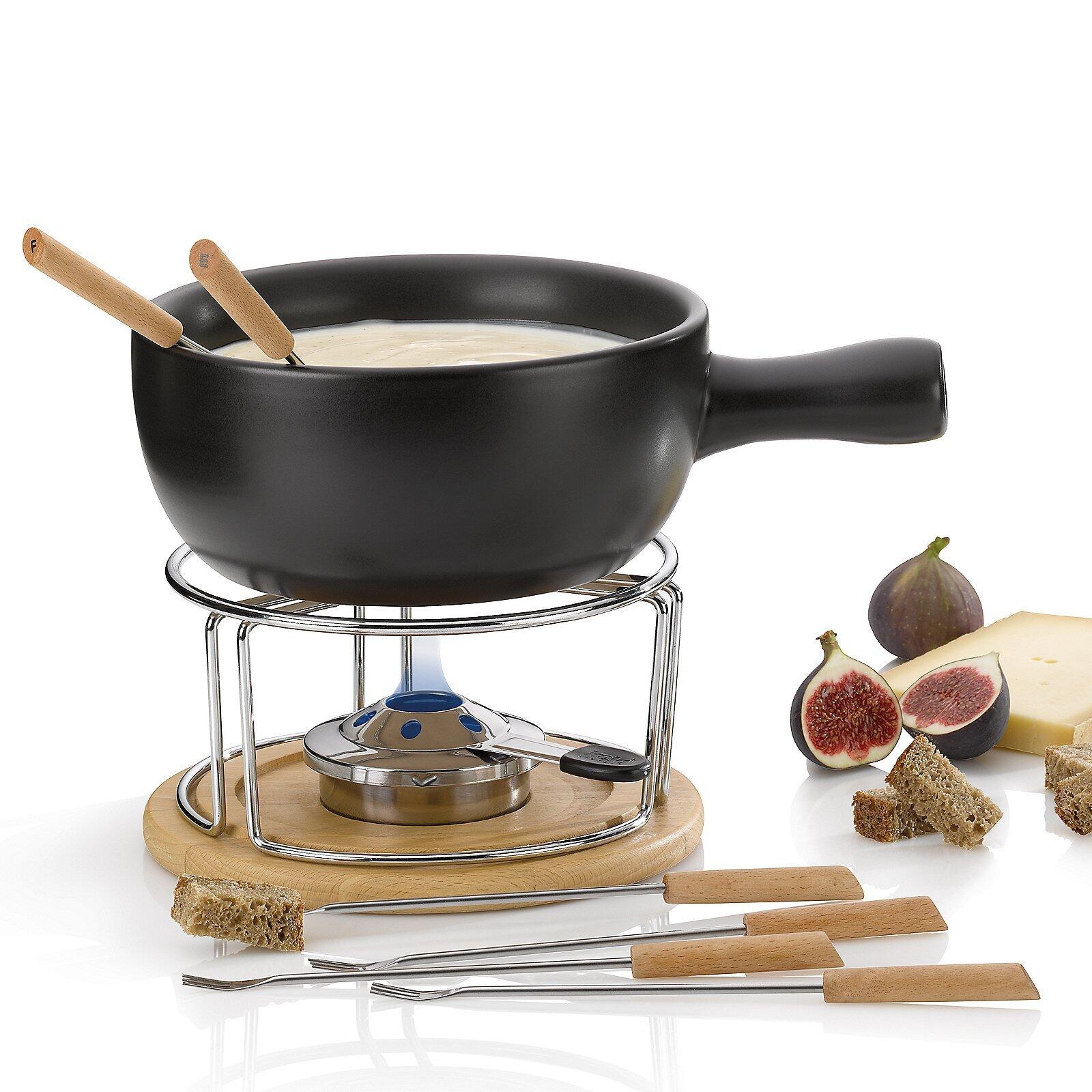 Fondue-Set Natura: Edelstahl-Fondue-Topf mit Holzgriff auf Brenner mit Bambus-Teller, umgeben von Fondue-Gabeln, Brot und Feigen, aus der Vogelperspektive.