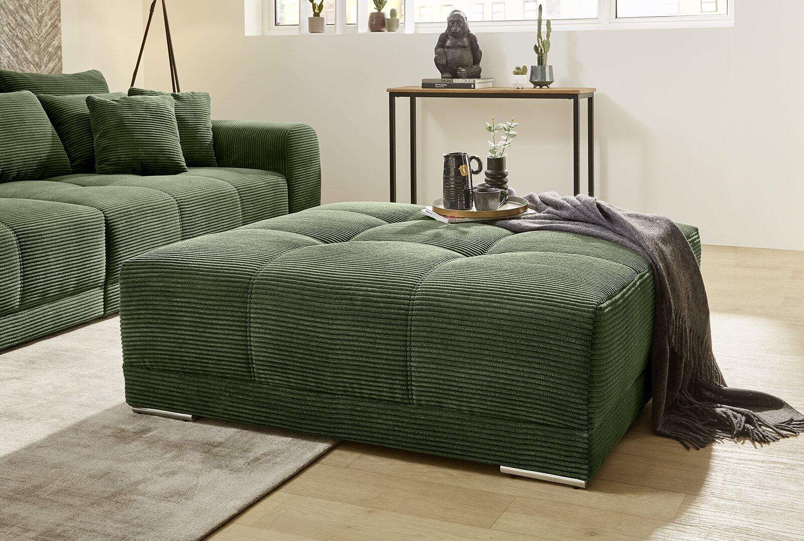 Grüner Hocker Moldau mit Cordbezug und Schachbrettmuster, präsentiert in einer Innenansicht mit passendem Sofa und Beistelltisch.