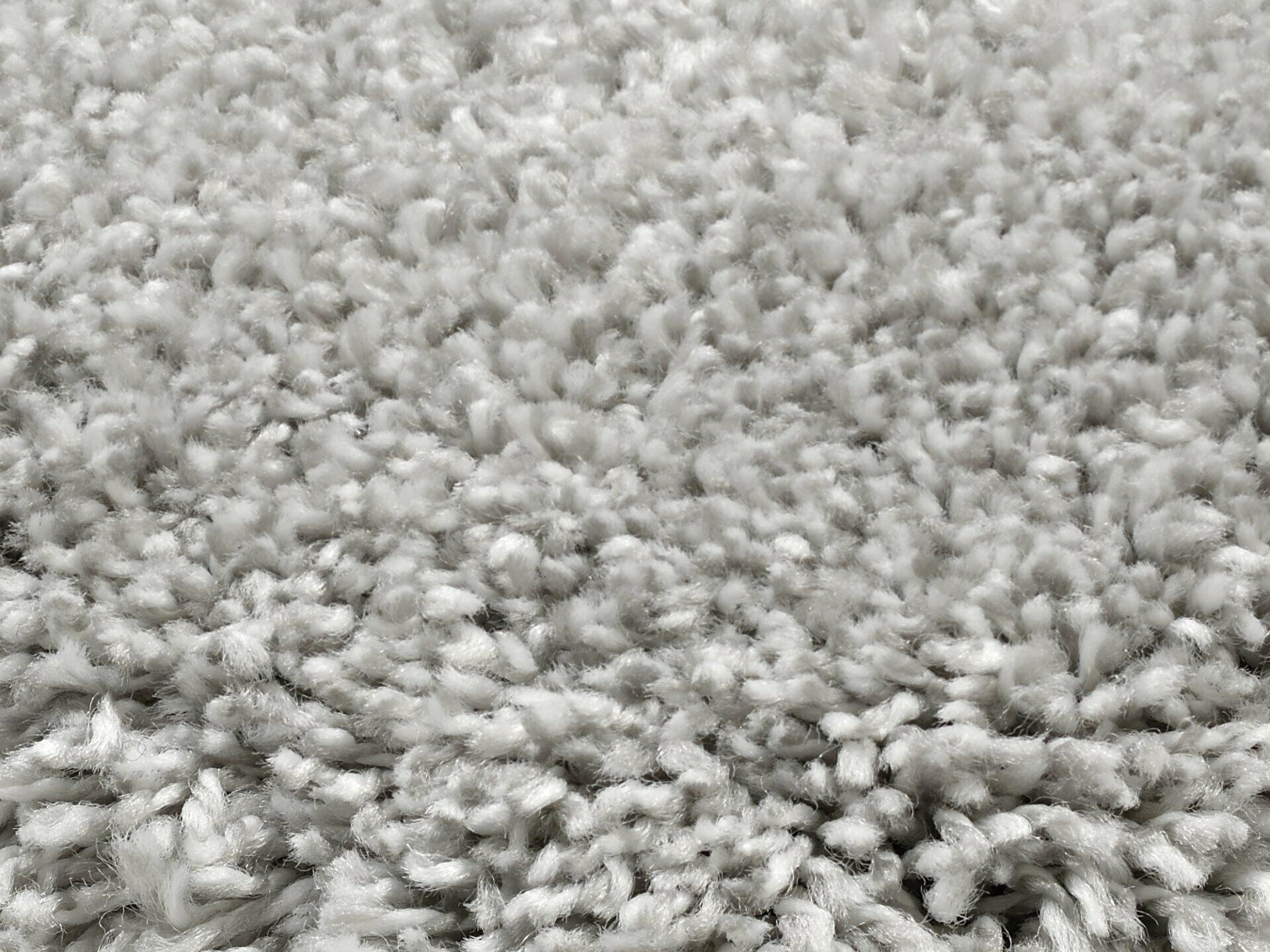 Nahaufnahme eines hellgrauen, flauschigen Hochflor-Teppichs der Modellreihe Erdara mit dichter, unregelmäßig hochstehender Fadenstruktur.