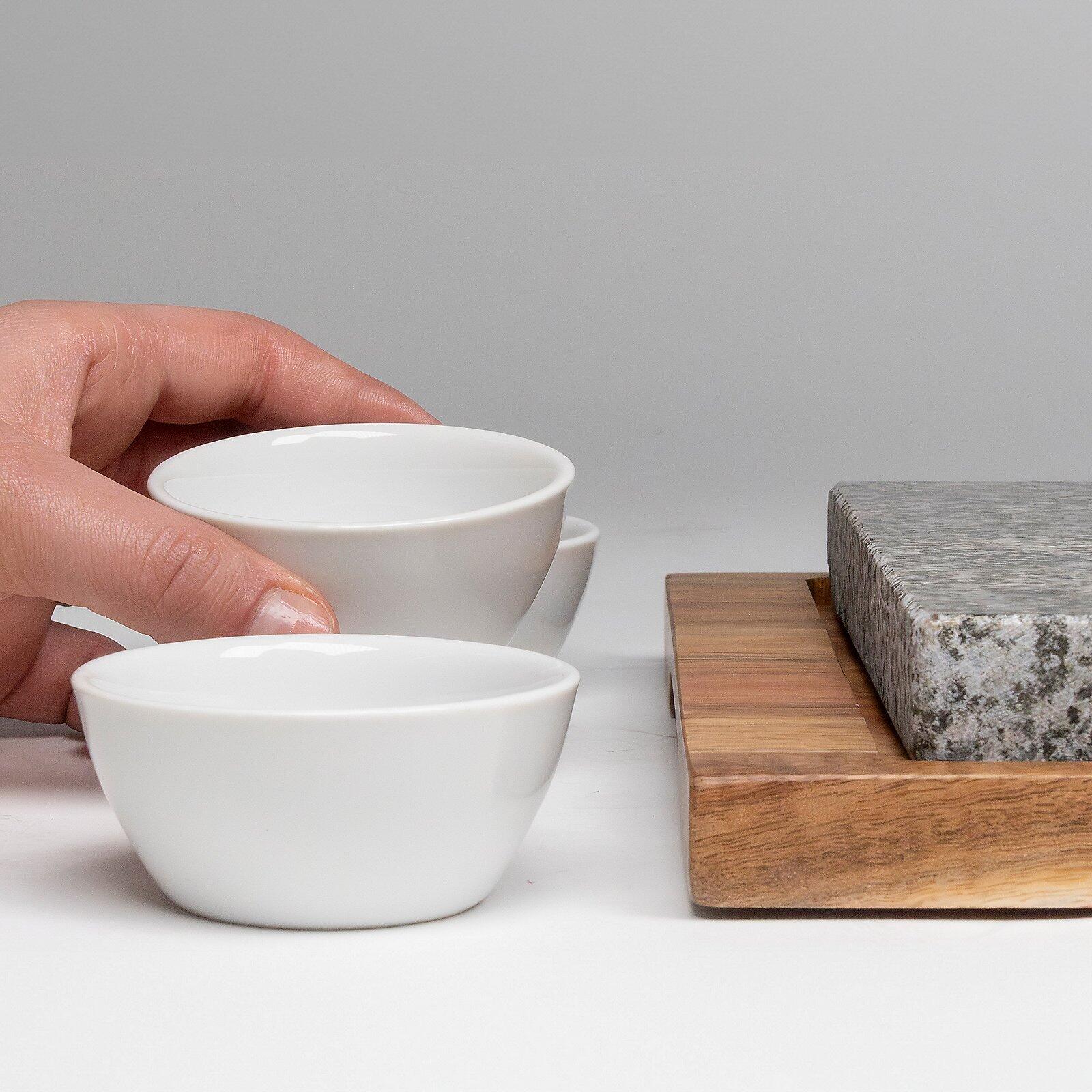 Keramische, schalenförmige Behälter aus weißem Material, wobei eine Hand einen der Behälter hält und die Form der Behälter durch die Perspektive von unten betont wird.