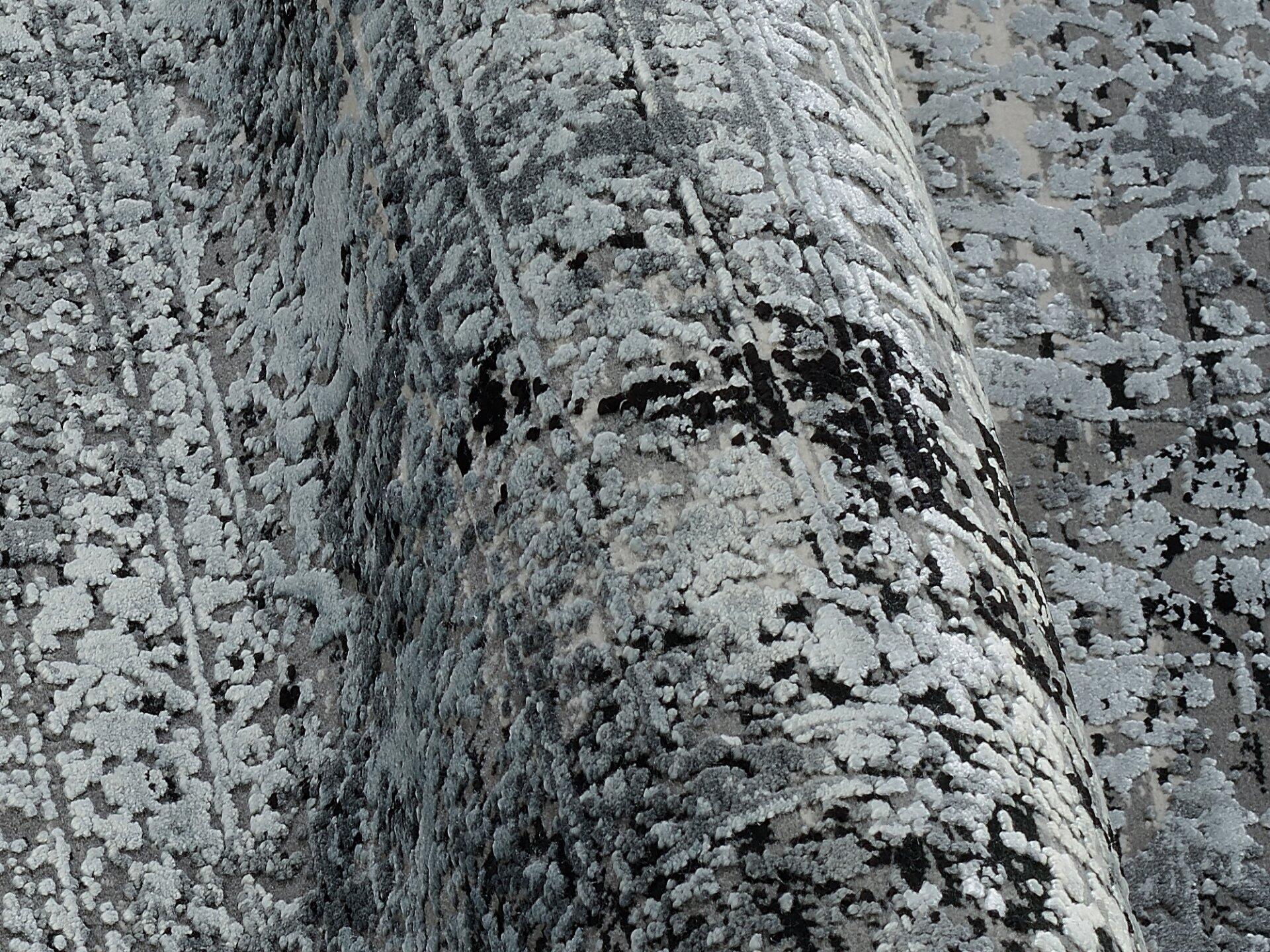 Detailaufnahme des Maschinenwebteppichs Thalorin mit strukturierter Oberfläche aus dunklen und hellen Bereichen und erhabenen Punkten.