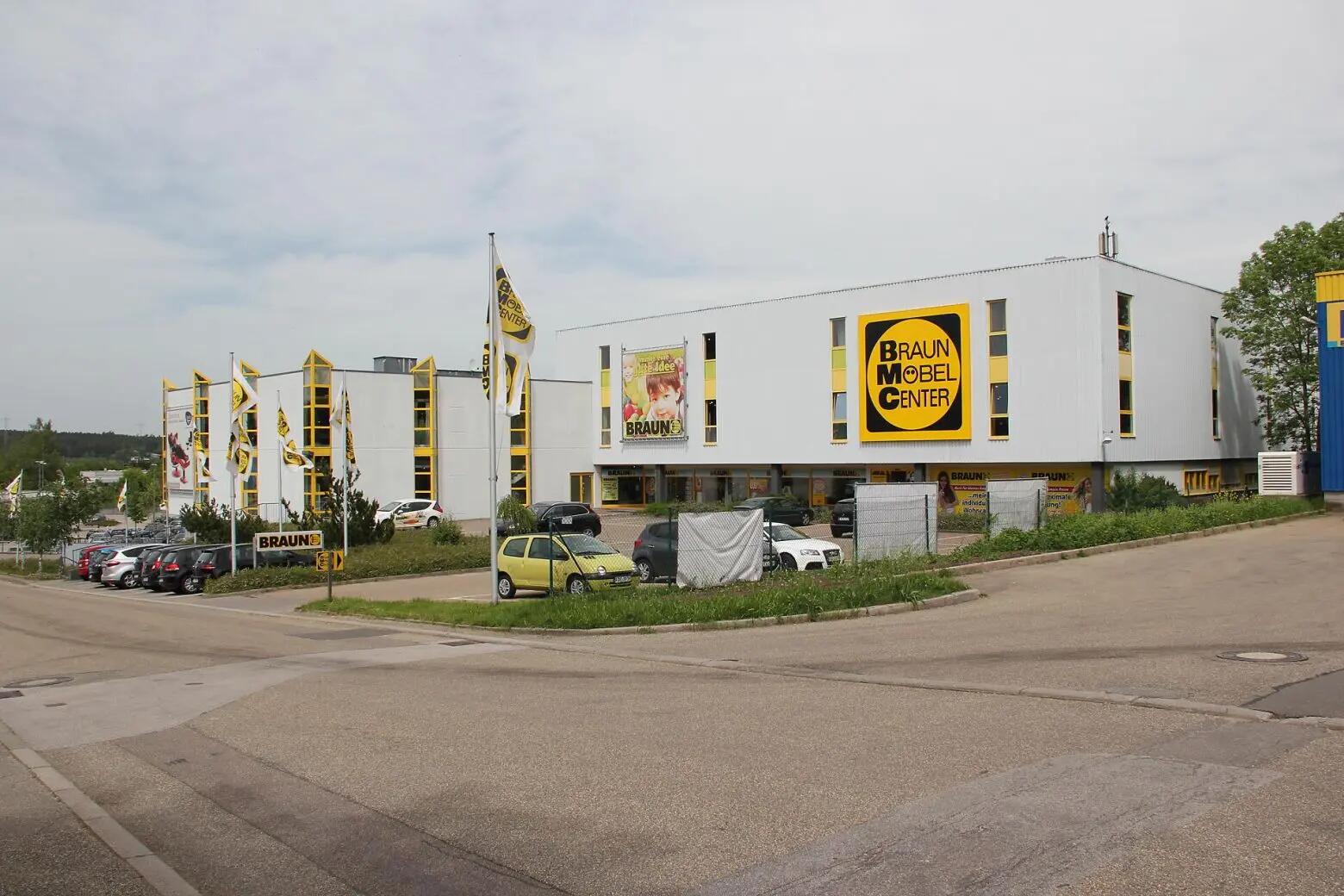 Braun Möbel Center mit moderner Architektur und Parkplatz, erkennbar an Fahnen und Schildern.