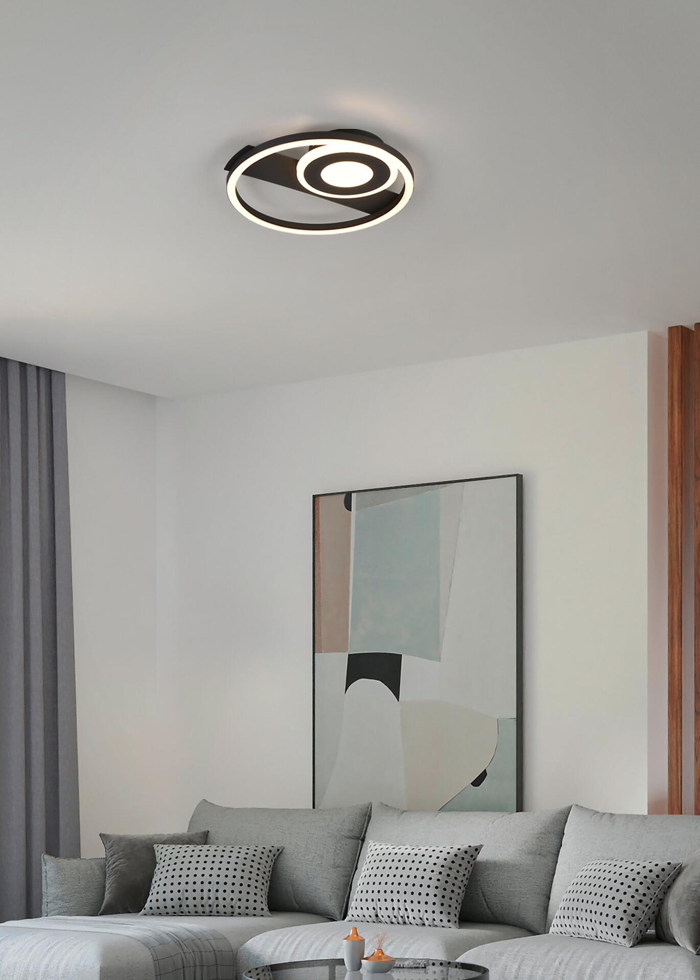 Deckenleuchte Horus mit kreisförmigem Design aus schwarzen und weißen Ringen, die von unten beleuchtet wird und warmes Licht in ein modernes Wohnzimmer wirft.