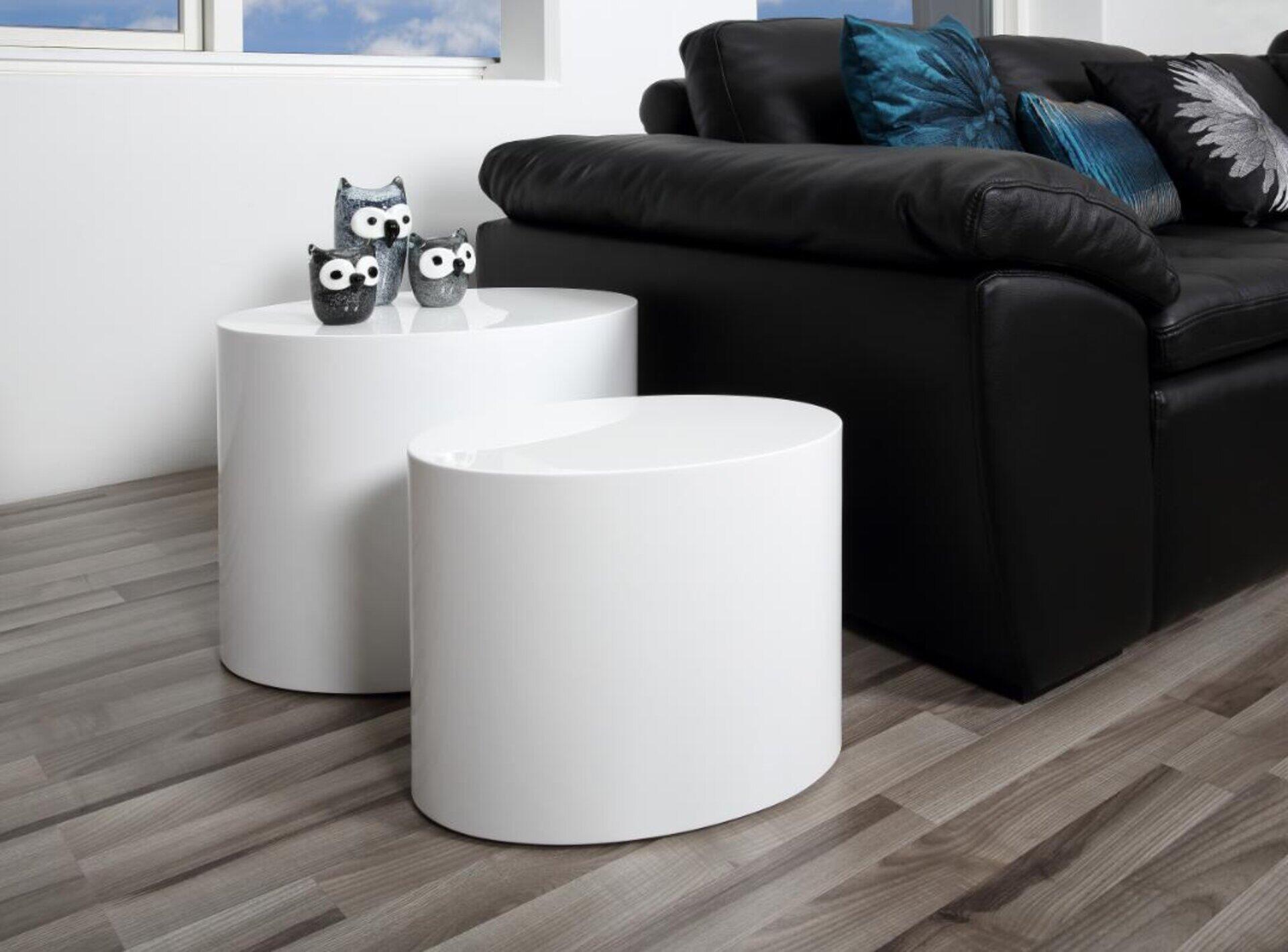 Zwei weiße, zylindrische Beistelltische aus der Mice-Serie, unterschiedlich hoch angeordnet und mit Deko-Eulen auf dem vorderen Tisch, als Teil eines minimalistischen Wohnambiente mit schwarzem Sofa.