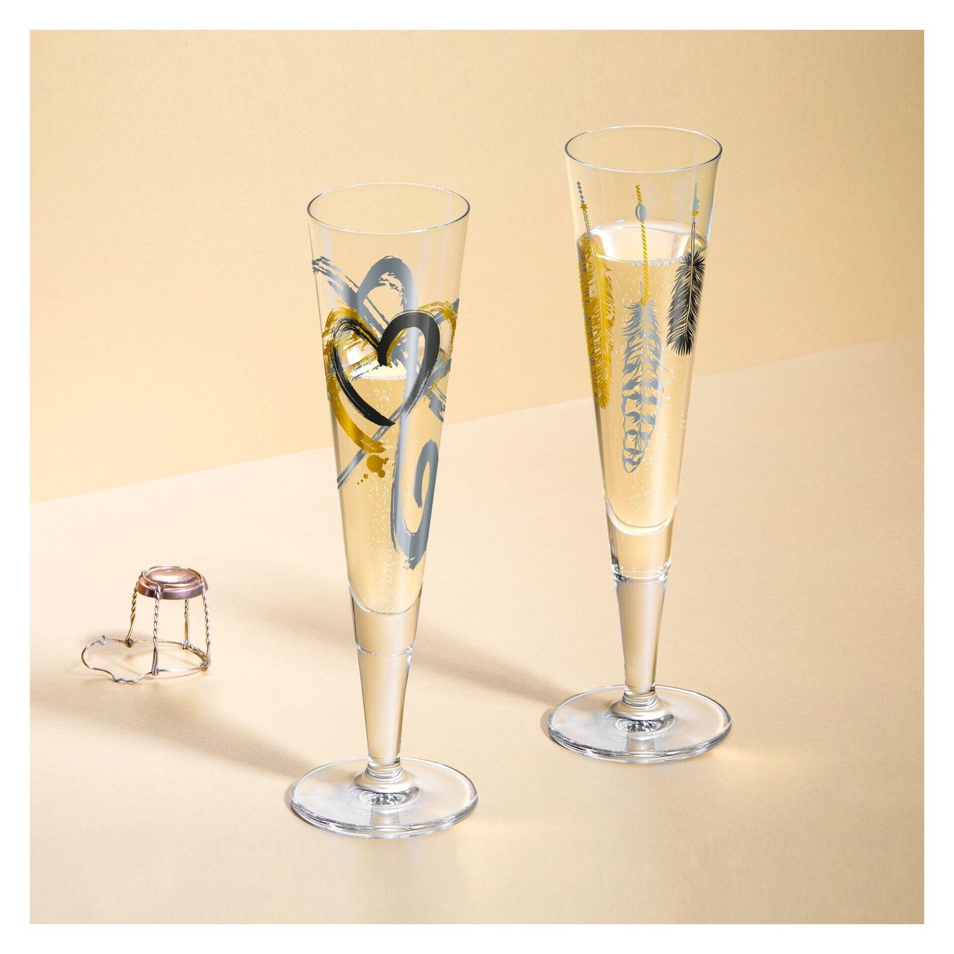 Zwei Champagnergläser mit goldenem Herz- und Federprint auf einer hellbeige Oberfläche, ergänzt durch einen silberfarbenen Champagnerflaschenöffner.