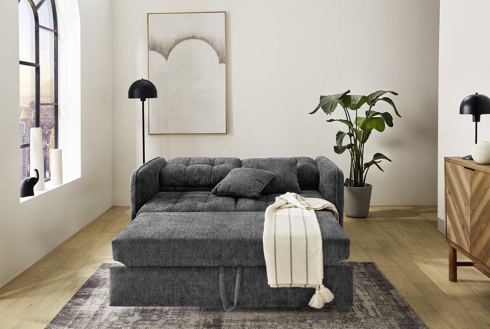 Schlafsofa Leon mit Relax- und Schlaffunktion, gezeigt aus erhöhter Perspektive in einem stilvollen Wohnzimmer mit Tagesdecke und Kissen.