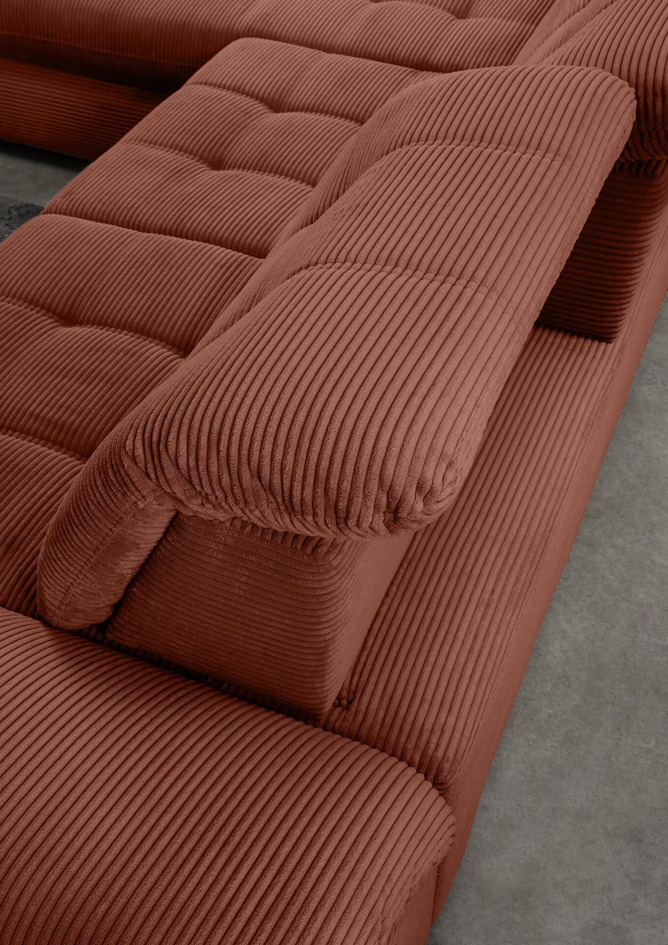 Nahaufnahme der Armlehne des Ecksofas Rigatti mit breiter Ablagefläche und auffälligem Cord-Rippenmuster in Rostrot.