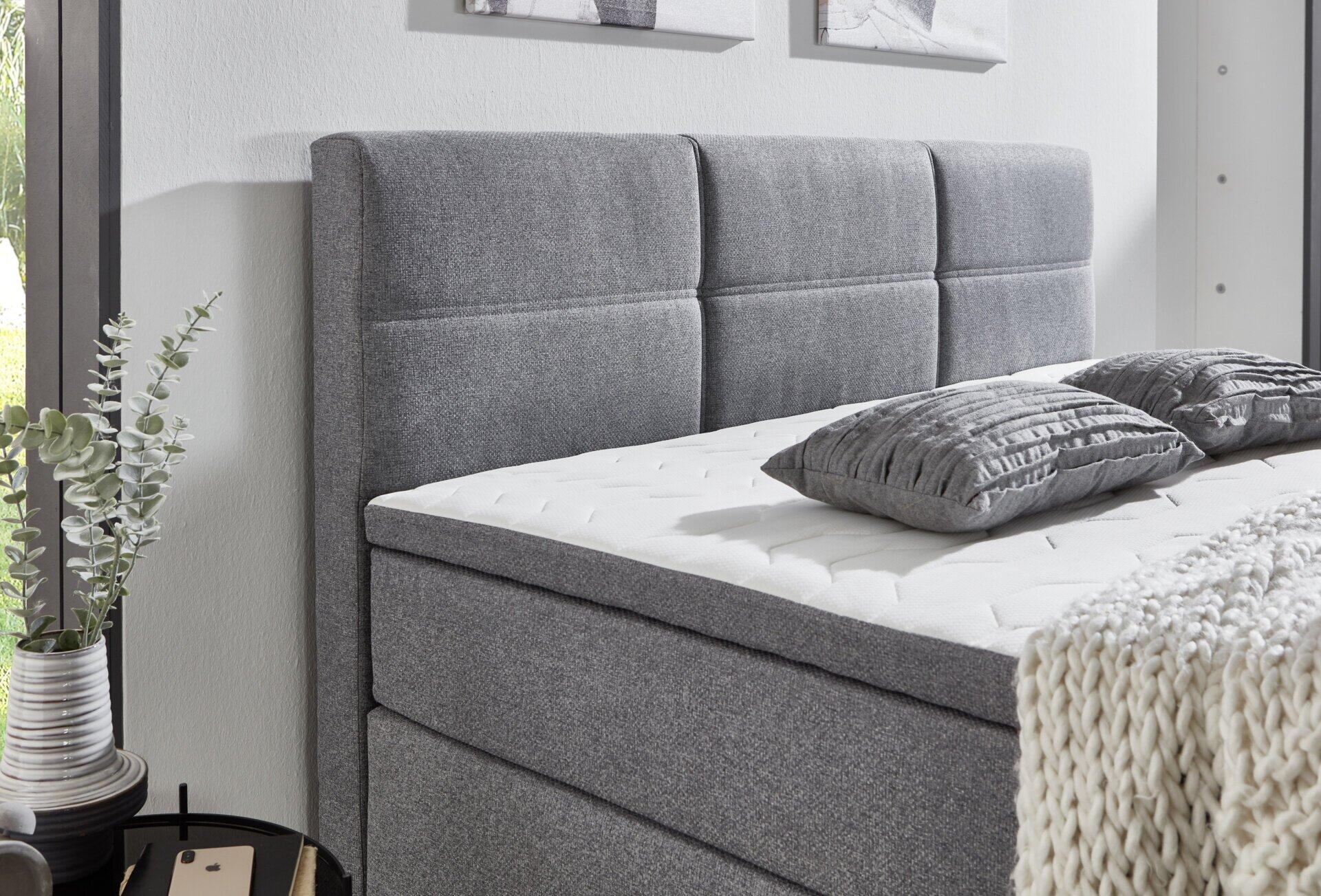 Boxspringbett Kenora BX2360 mit grauem, gepolstertem Bettkopfteil und integriertem Bettkasten, seitlich aus Dreiviertelperspektive dargestellt.