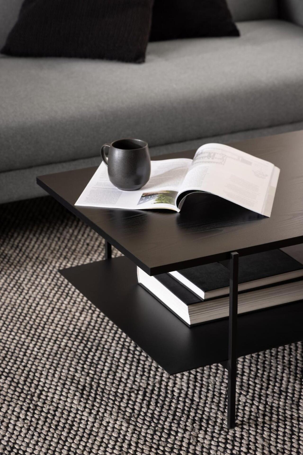 Couchtisch Angus mit rechteckiger Form und integriertem Regal, präsentiert aus leicht erhöhter Perspektive mit dekorativen Elementen auf der Tischplatte.
