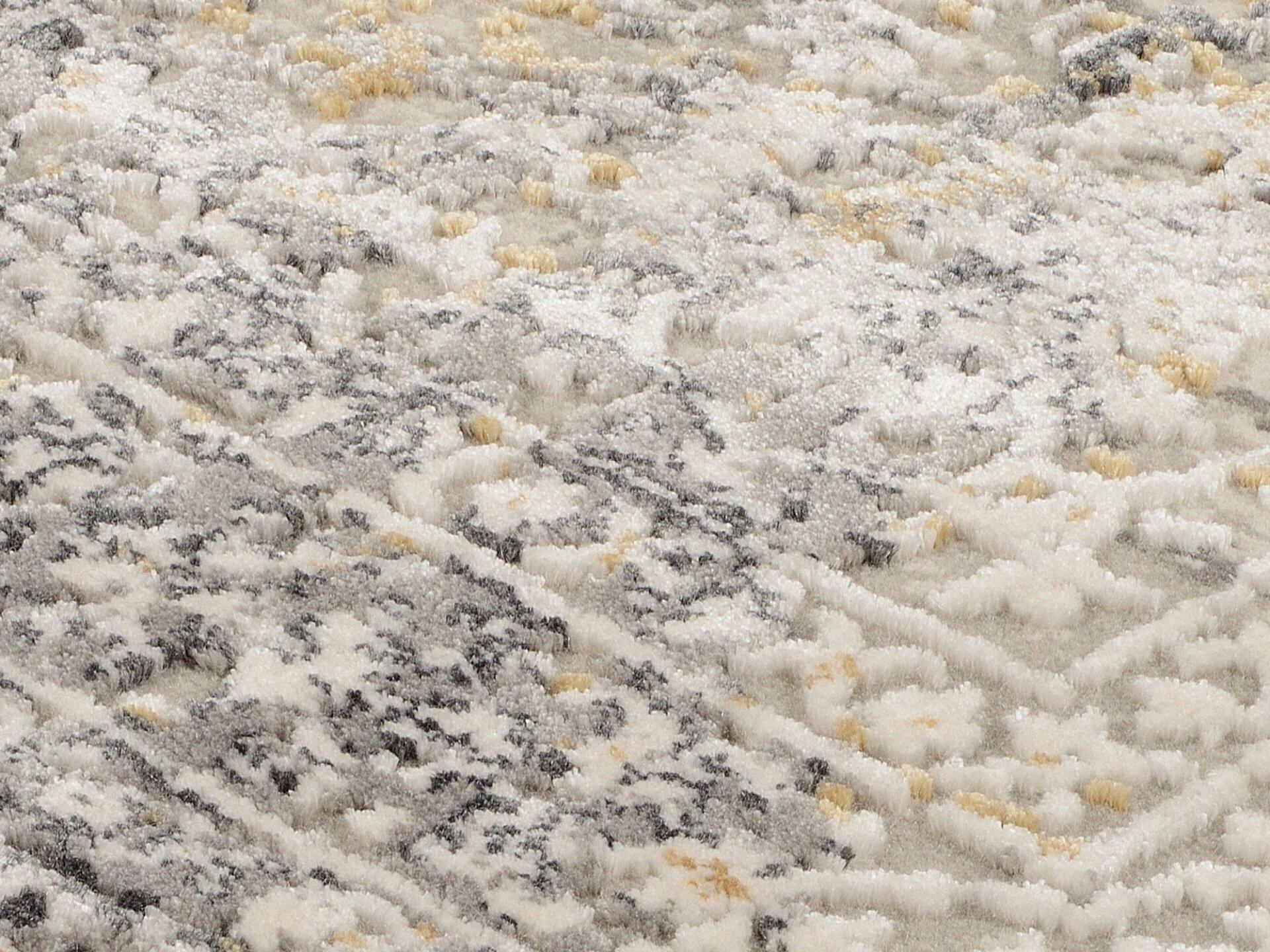 Nahaufnahme des Maschinenwebteppichs Amasya mit erhabenem, abstraktem Muster aus Viskose und Polyacryl in Creme, Grau, Schwarz und Gelb, das die flauschige Textur des Teppichs betont.