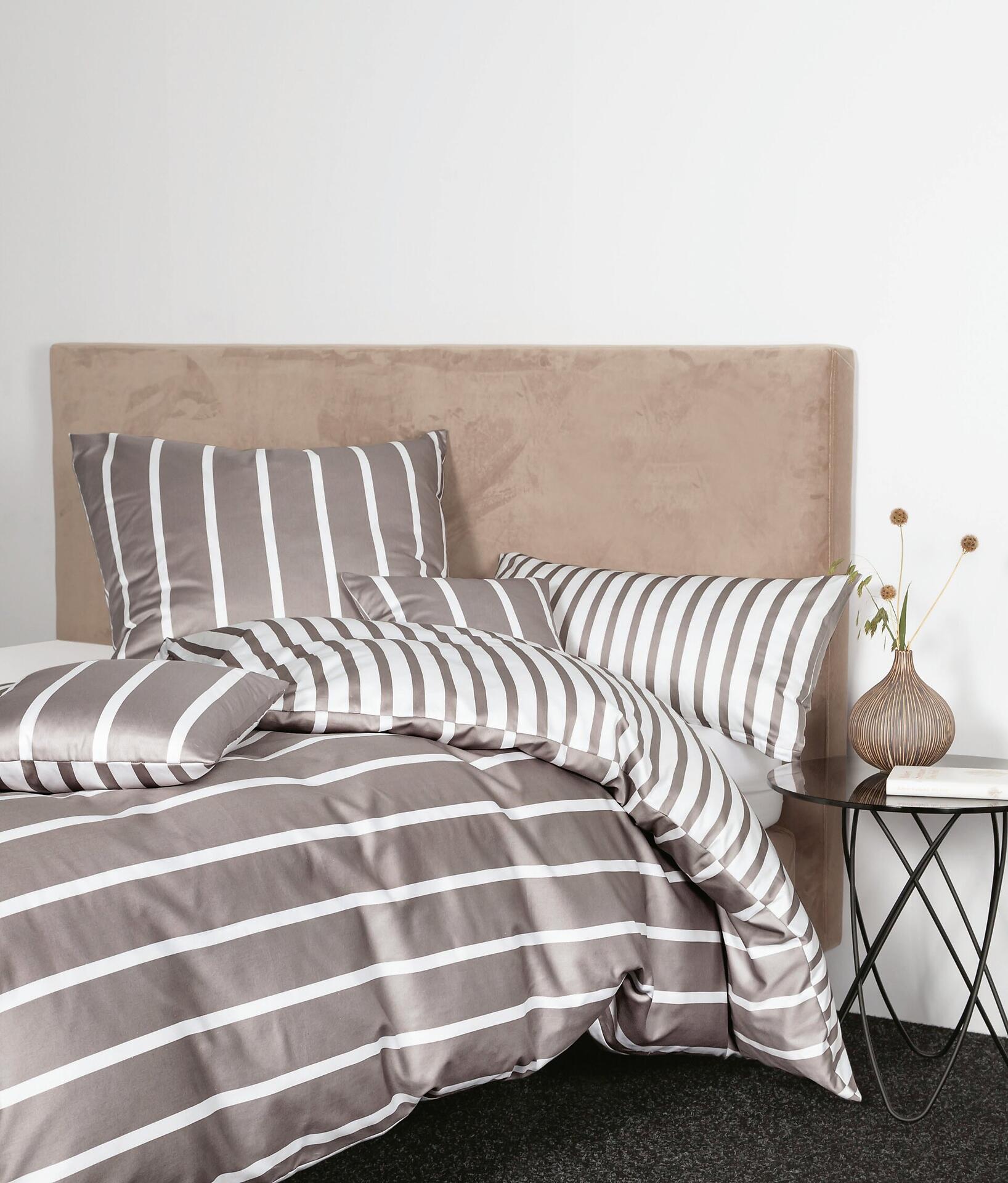 Bettwäsche modernclassic aus Mako-Satin-Baumwolle mit grau-weißem Streifenmuster, detailliert aus Perspektiv-Aufnahme mit locker drapierten Kissen und Kopfende.
