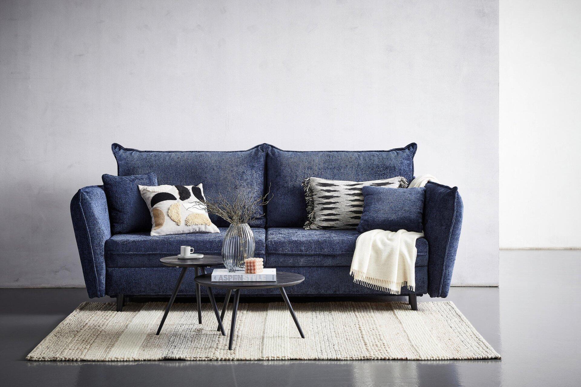 Dunkelblaues Sofa Santana mit hohem Rücken, leicht abgerundeten Armlehnen und drei Kissen auf einer breiten Sitzfläche, ergänzt durch dekorative Kissen und Stricküberwurf.