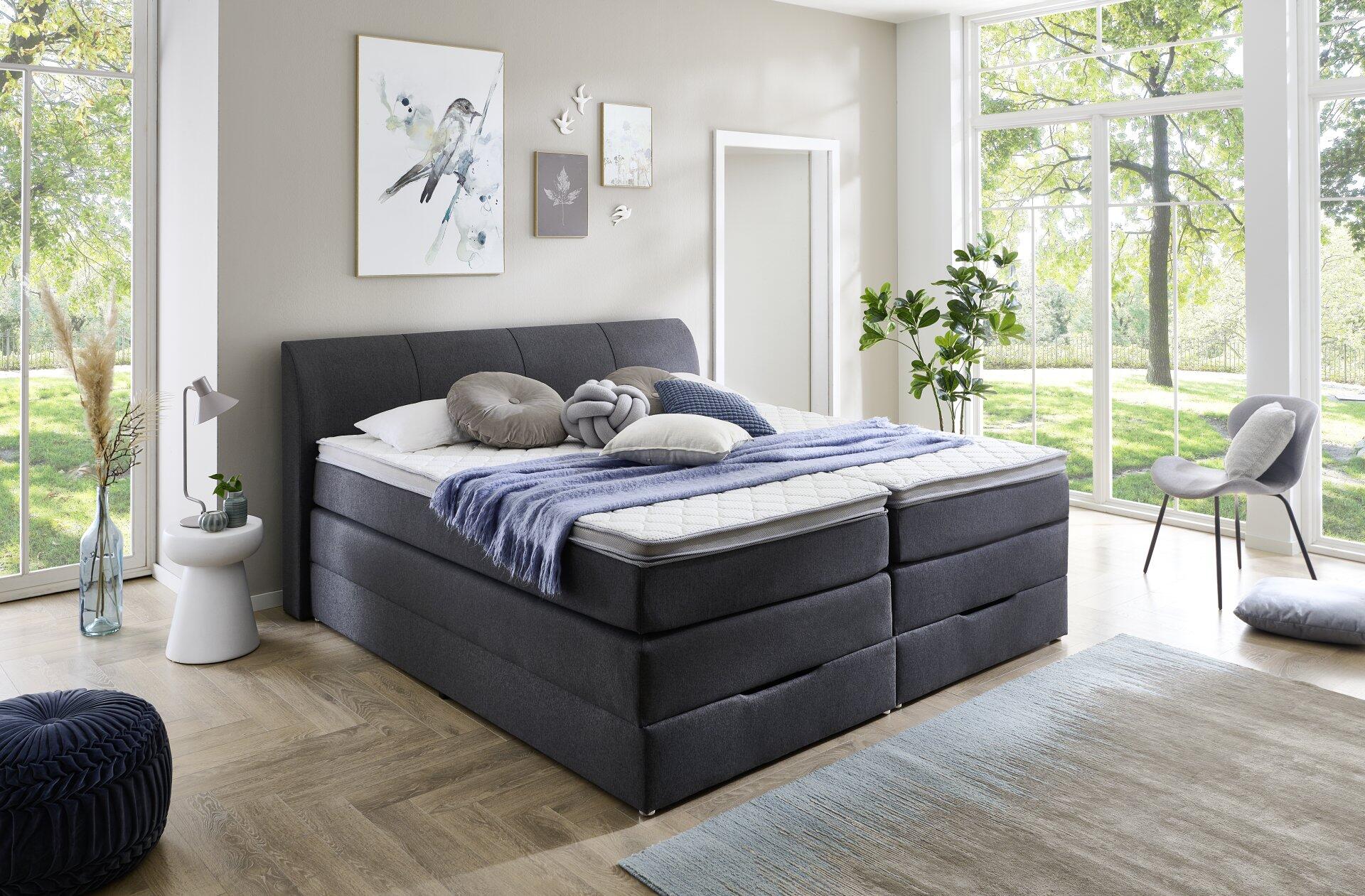 Boxspringbett Modesto BX1440 mit grauem Bezug, integriertem Bettkasten mit Schubladen und Tageslichtperspektive.