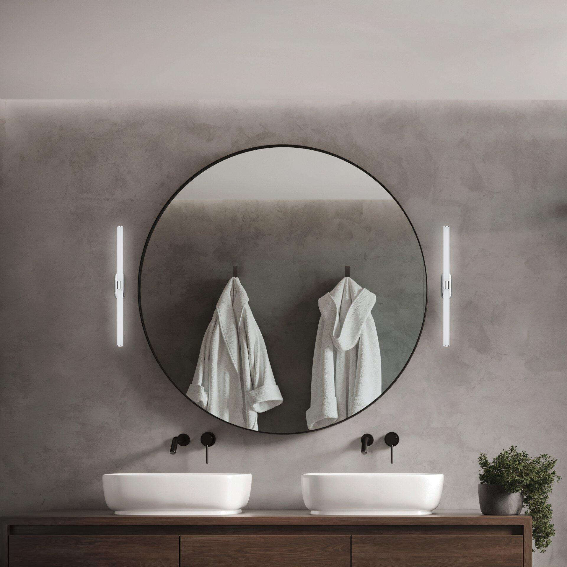 Wandmontierte Badezimmerleuchte Runt mit diffuses Licht, flankierend einen runden Spiegel mit schwarzem Rahmen, in einem modernen Badezimmerambiente.