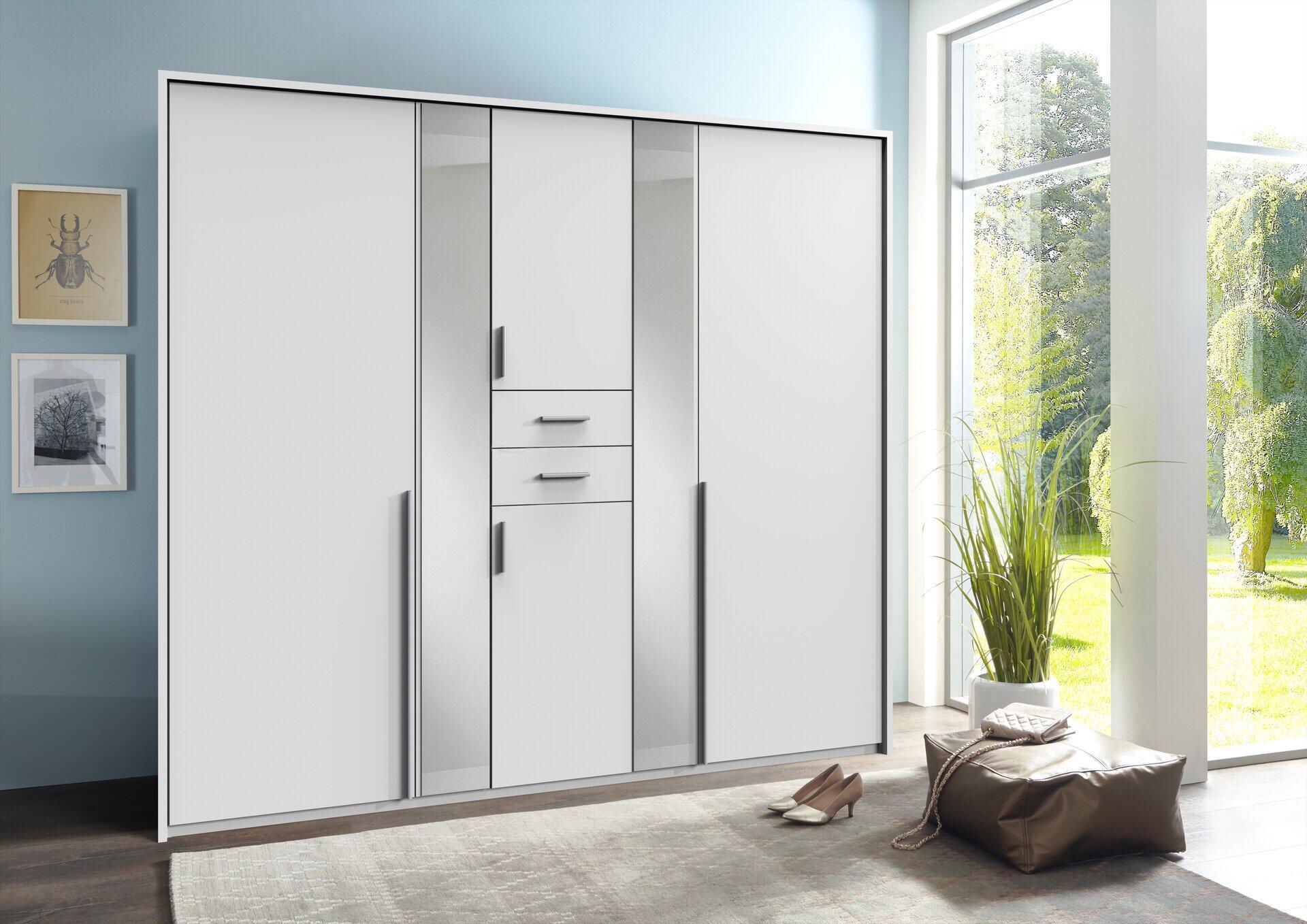 Weißer Kleiderschrank Vanea mit fünf Schiebetüren, vertikalen Griffmulden und Schubladen, der an einer Wand in einer modernen Wohnung steht.
