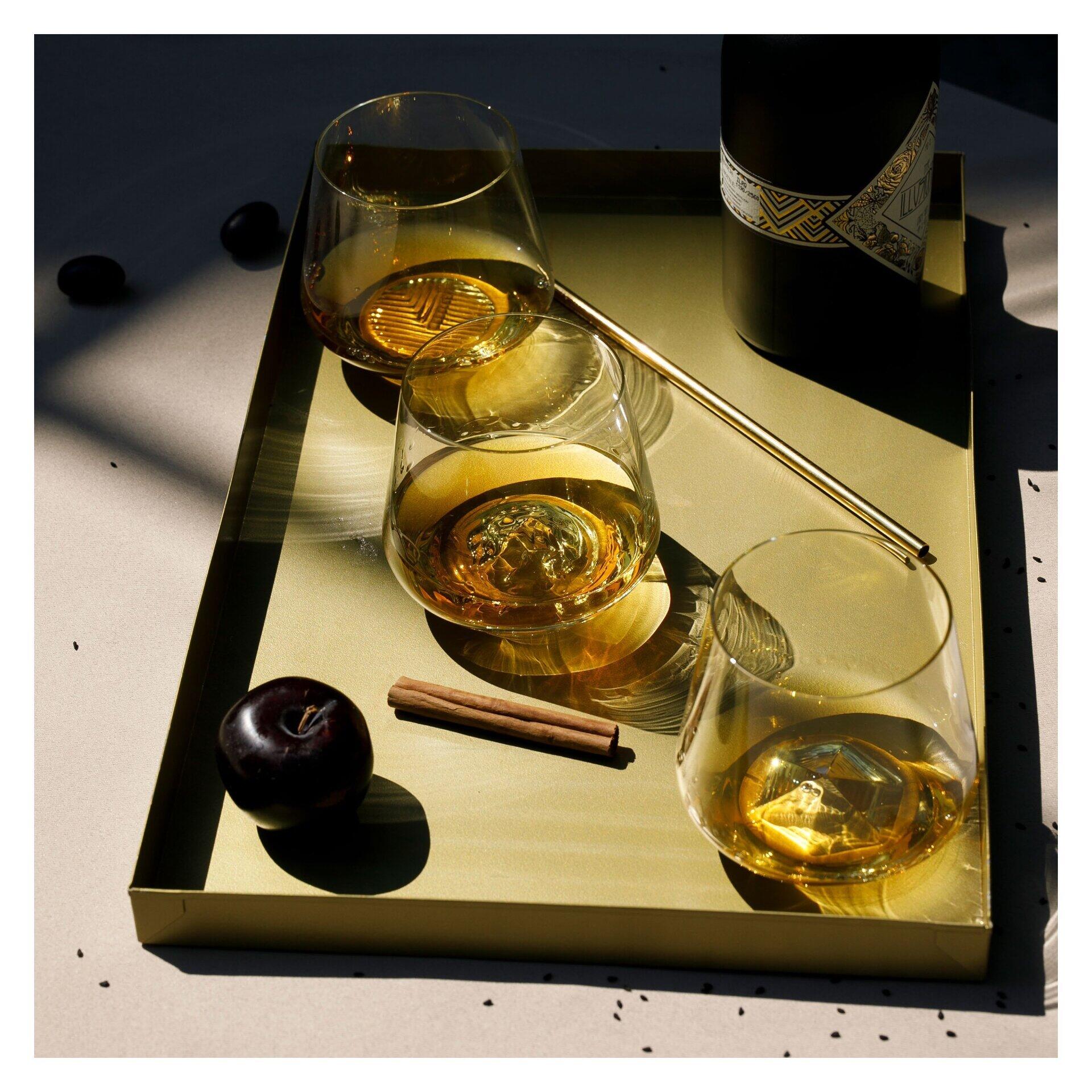 Whisky Tumbler in Geschenkbox auf goldenem Tablett, präsentiert mit Whisky, Zimt und Pflaume, aufgenommen aus schräg oben zur Betonung des stilisierten Arrangements.
