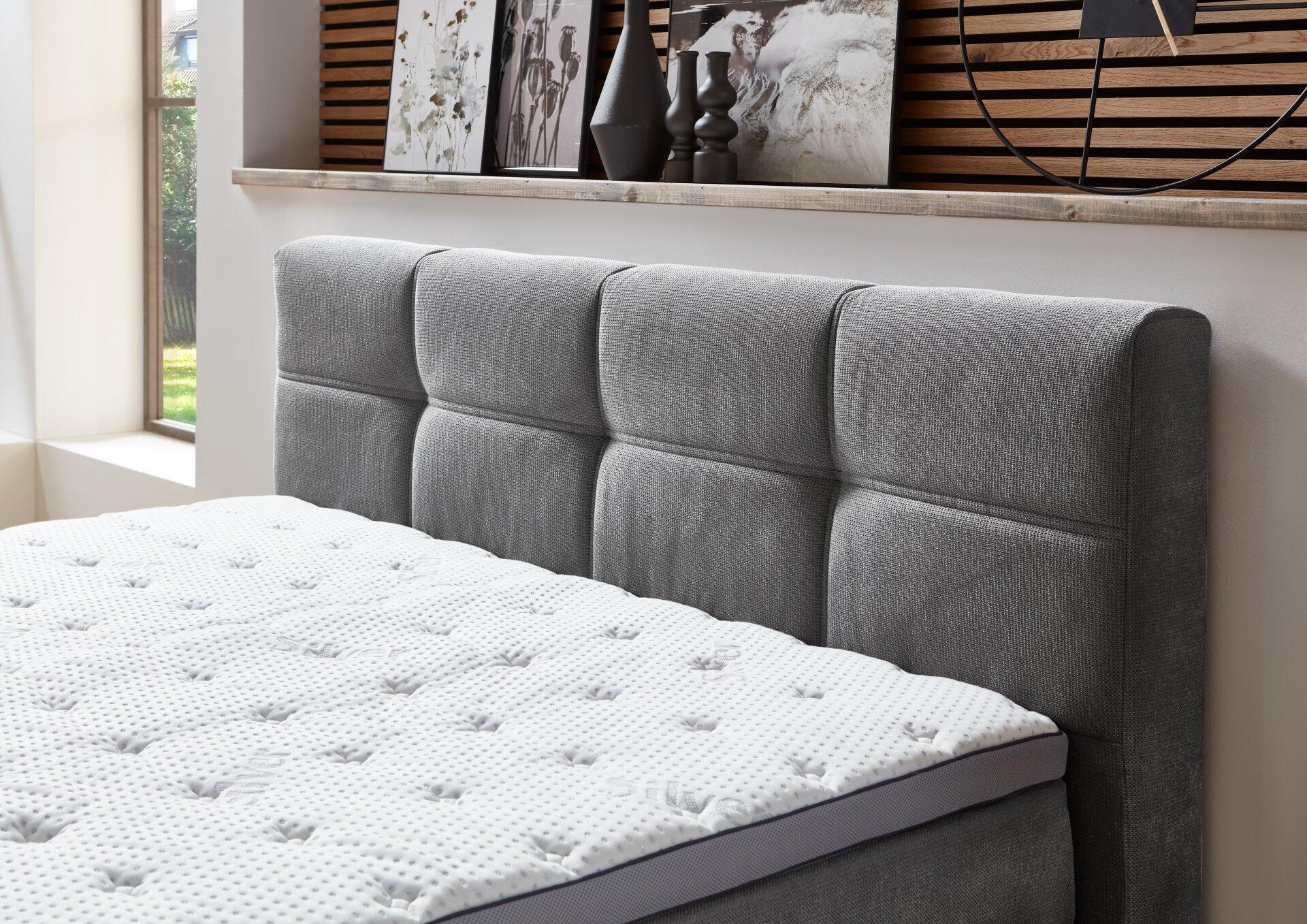 Boxspringbett Portage BX2110 mit grauem, gepolstertem Kopfteil mit vertikaler Faltung und integriertem Bettkasten.