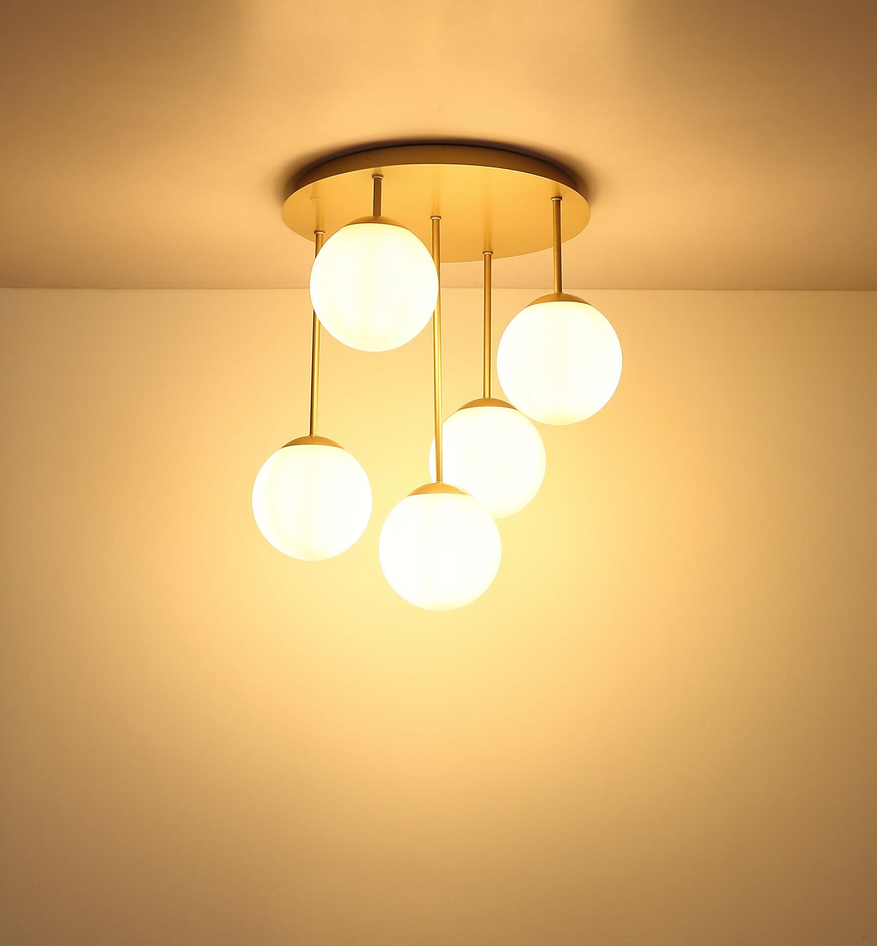 Deckenleuchte HARMON mit fünf weißen Glaskugeln in unterschiedlichen Längen, die von einer goldenen Basis hängen und ein warmes Licht abstrahlen.