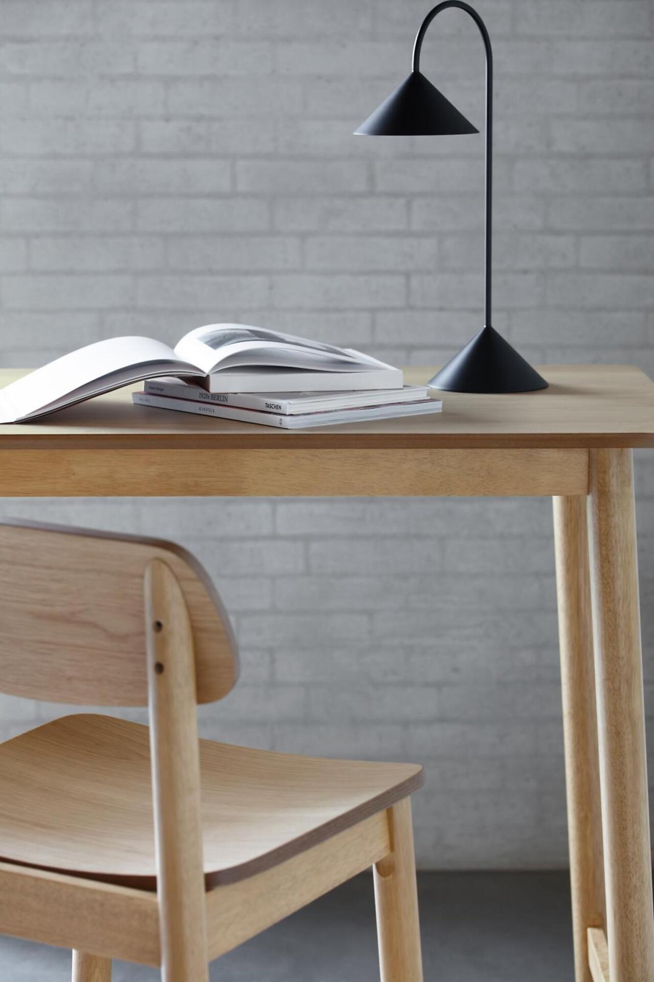 Bartisch Barlow mit Tischlampe, Büchern und Stuhl vor Ziegelwand.